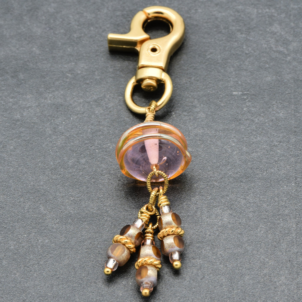 Gold charm with pink and ivory beads on a gray background