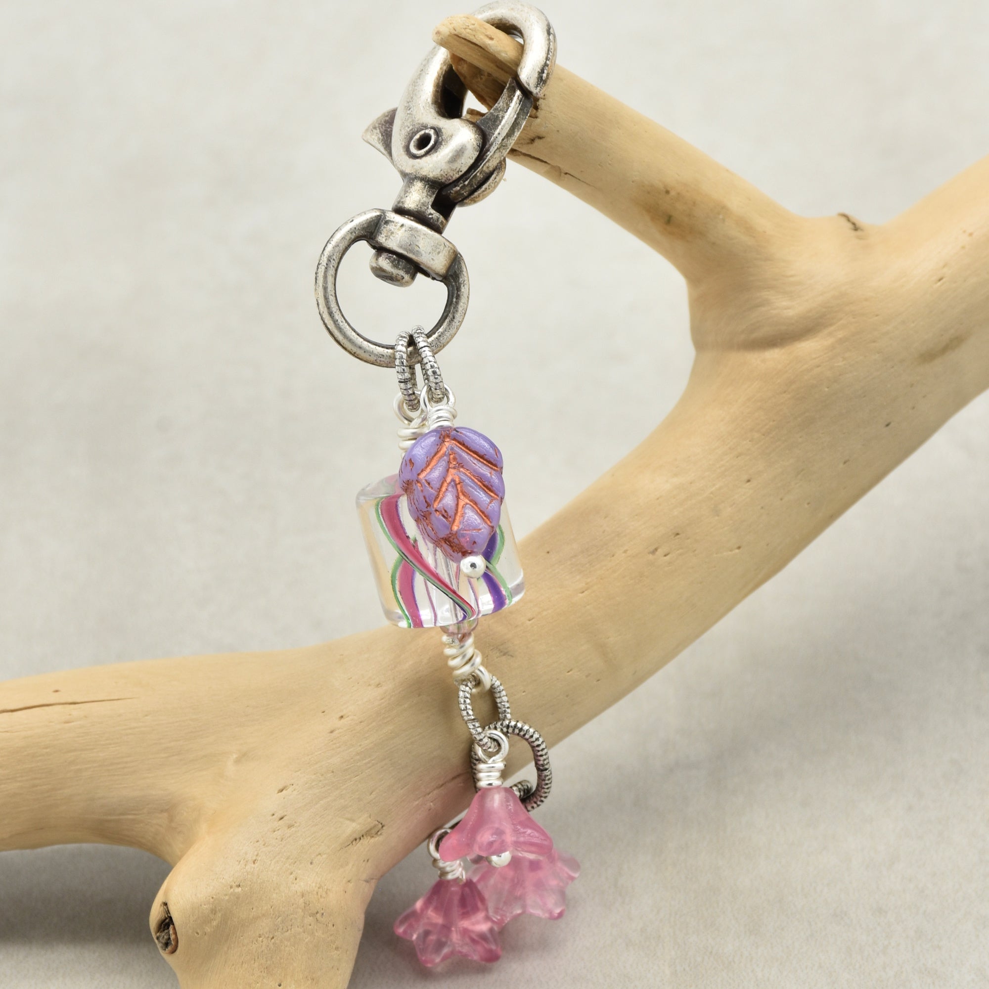 Keychain with pink floral charm and silver clasp on a wooden branch