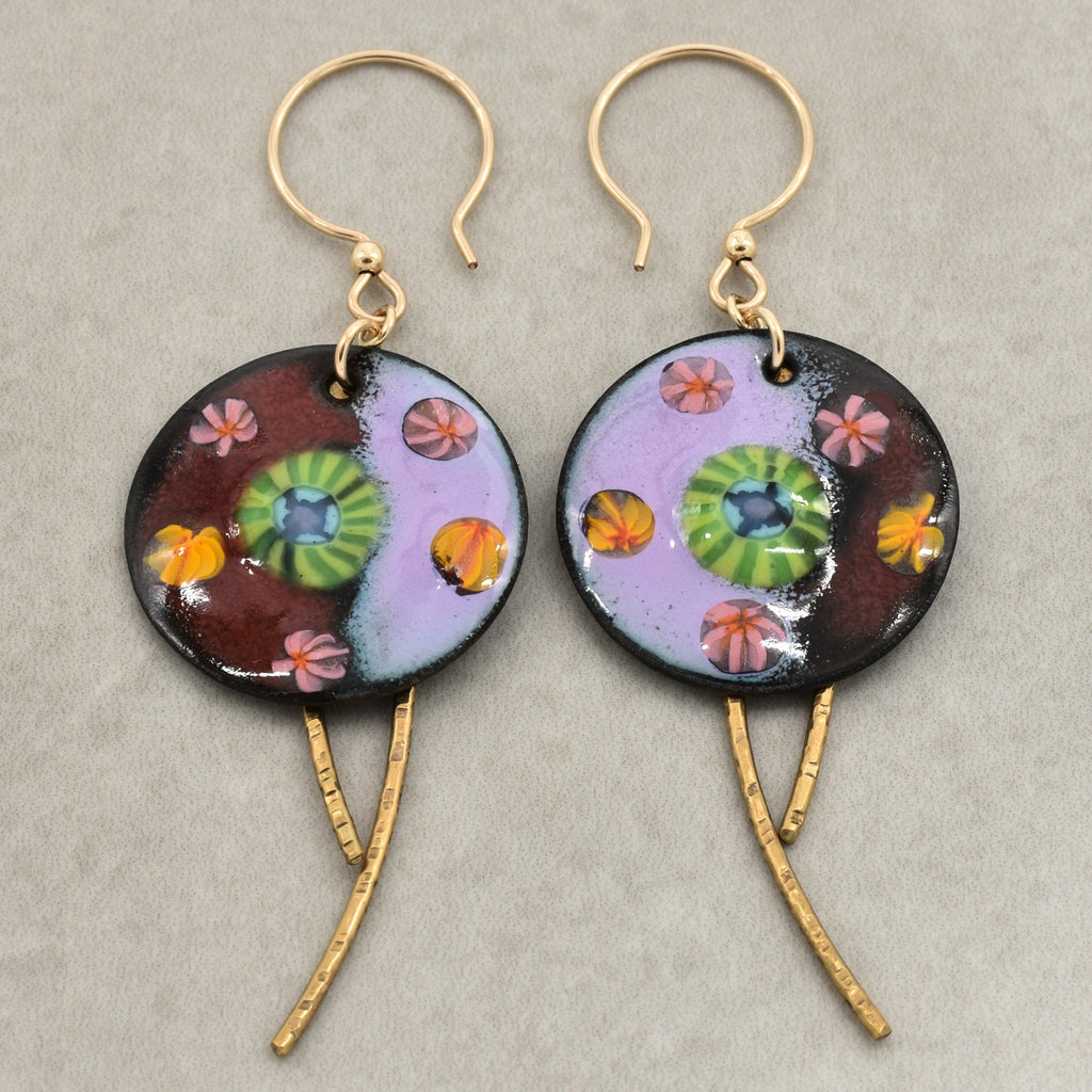 A pair of handmade enamel earring pendants with gold-tone ear wires and brass textured daggers, featuring a colorful Millefiori pattern on a light background - made with love in Colorado by Ruby Acorn.