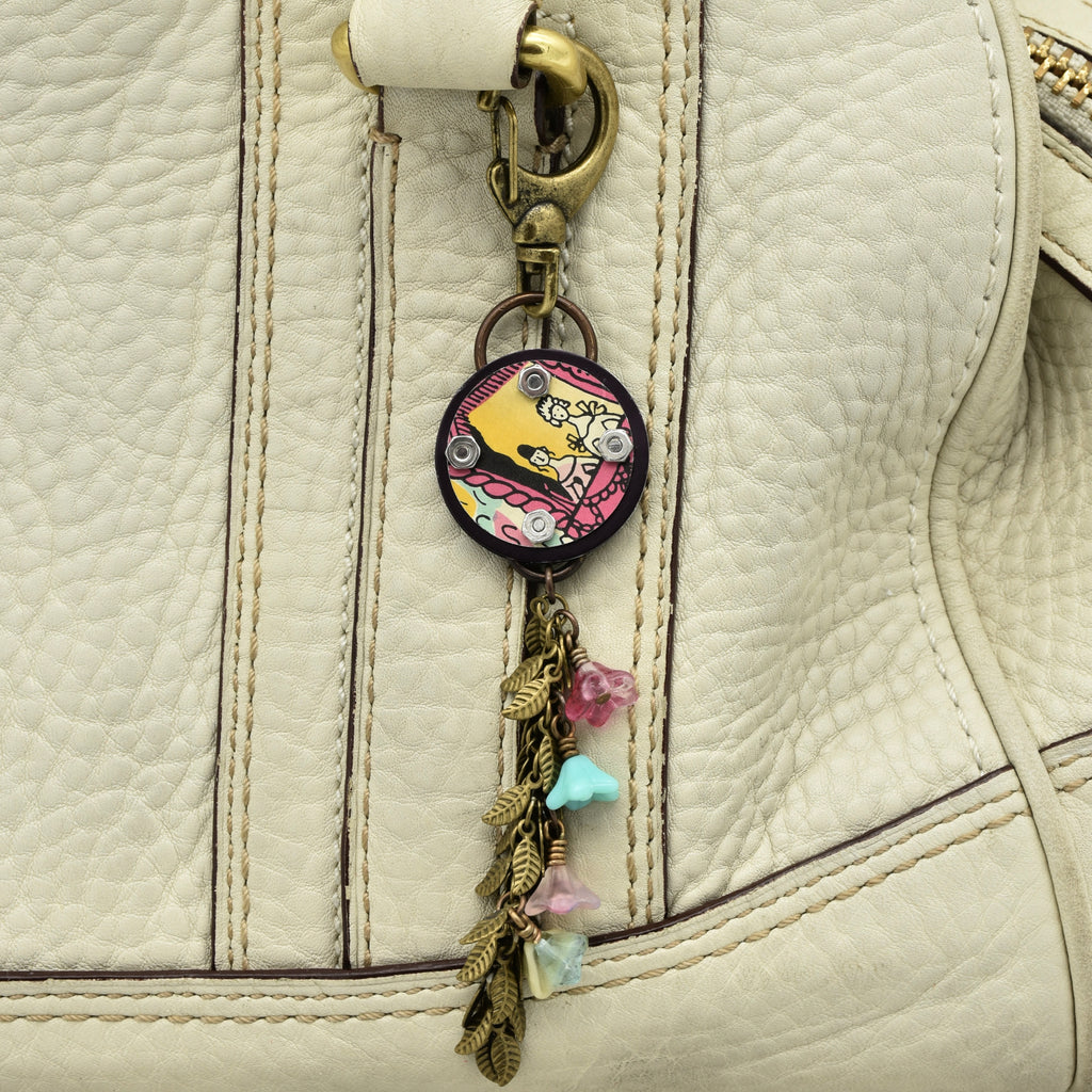 Handbag charm with colorful design attached to a beige leather bag