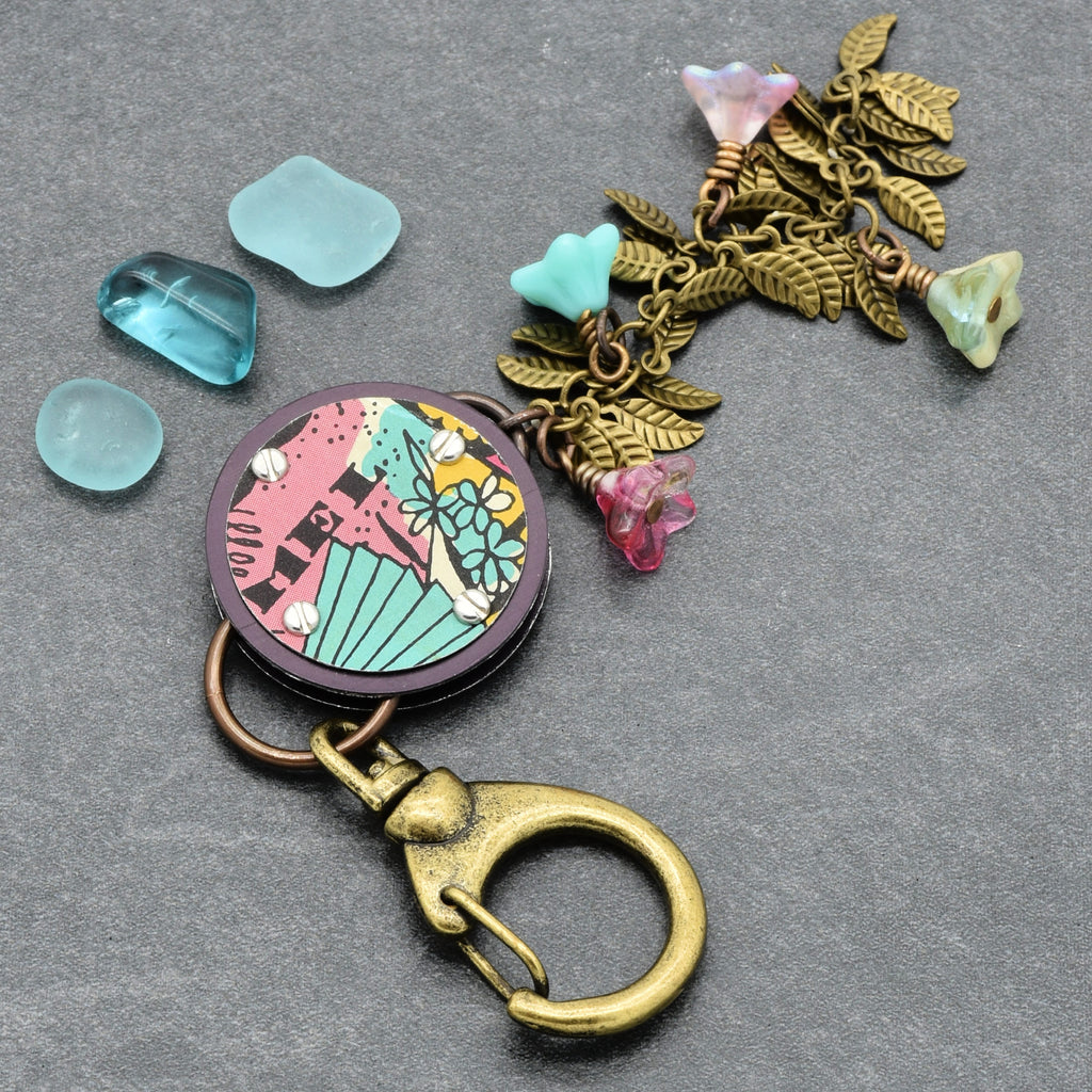 Decorative handbag charm with colorful pendant and floral charm on a gray background