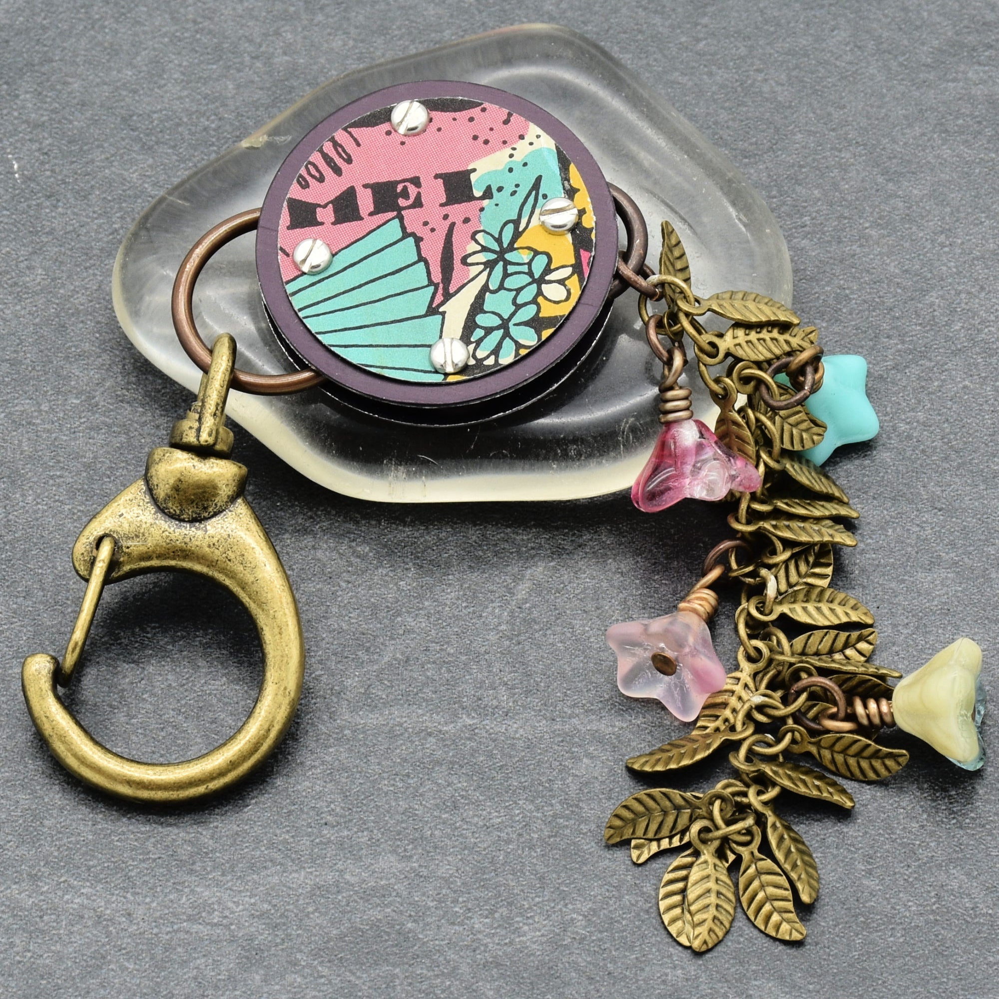 Decorative handbag charm with floral design and leaf details on a gray background