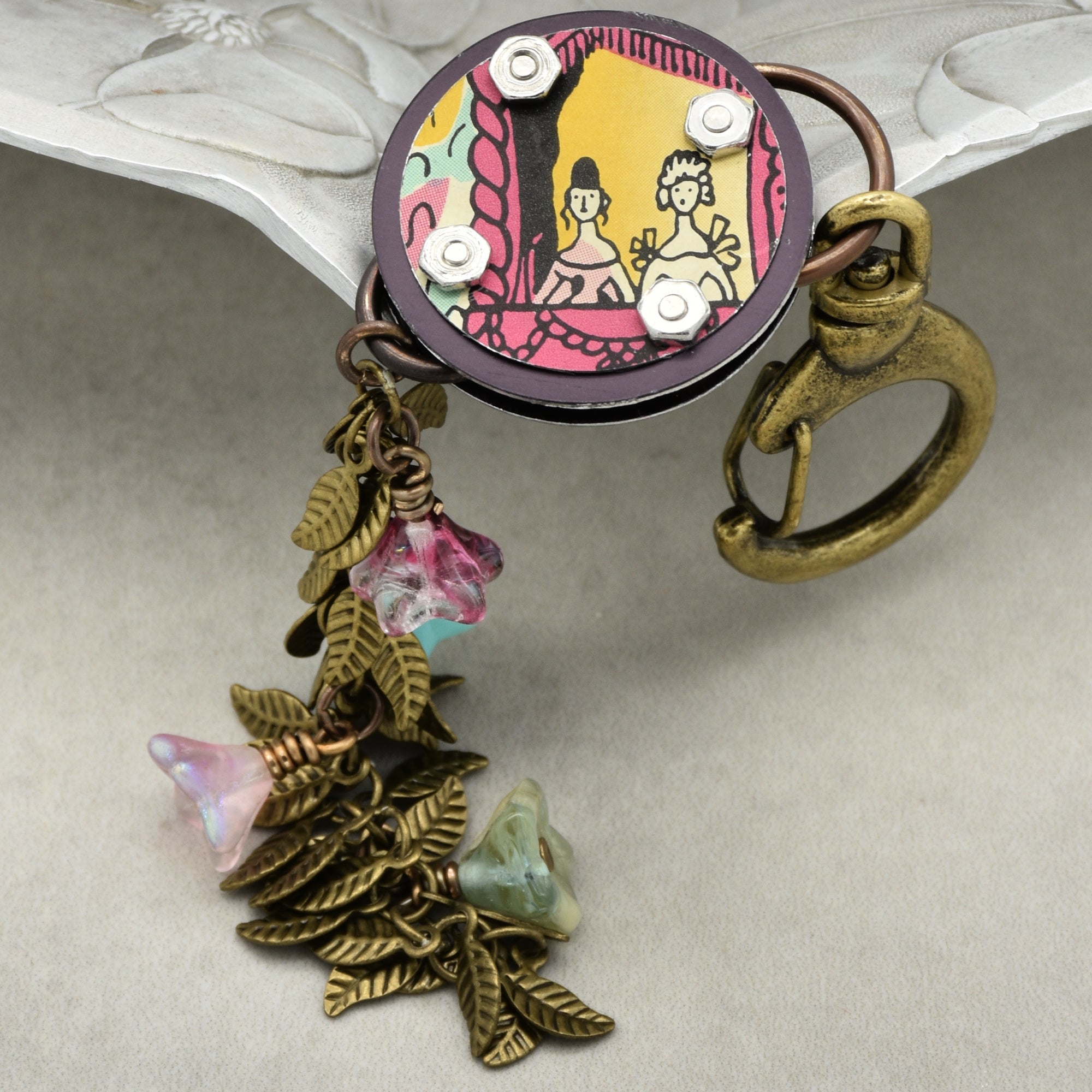 Decorative handbag charm with colorful design and leaf-shaped charms on a light background