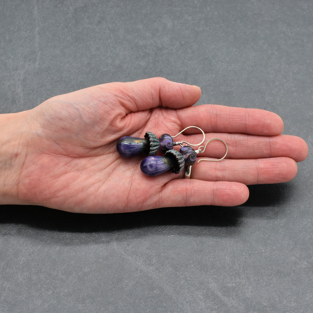Hand holding a pair of purple beaded earrings against a gray background