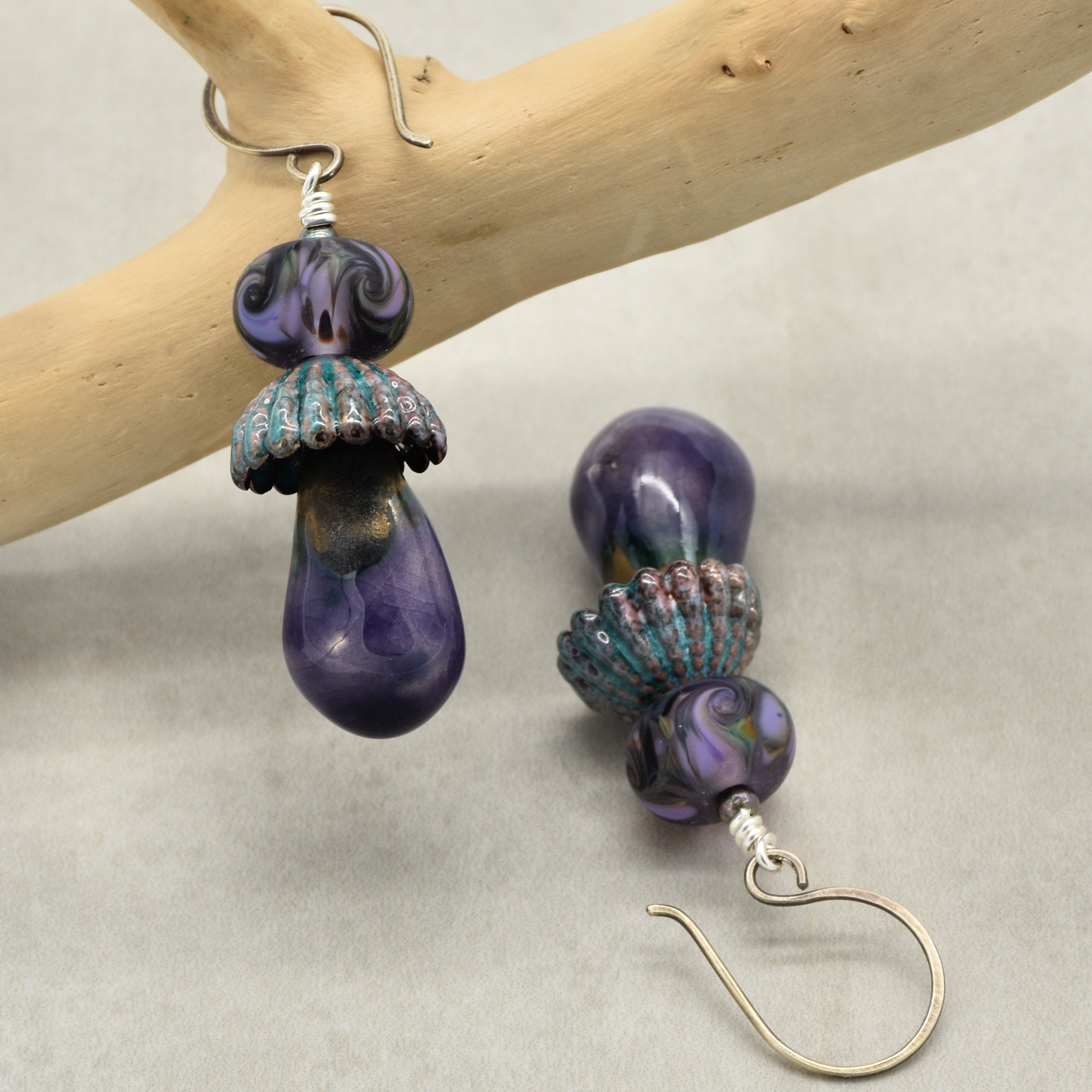 Pair of purple and teal beaded earrings on a light gray background with a wooden branch.