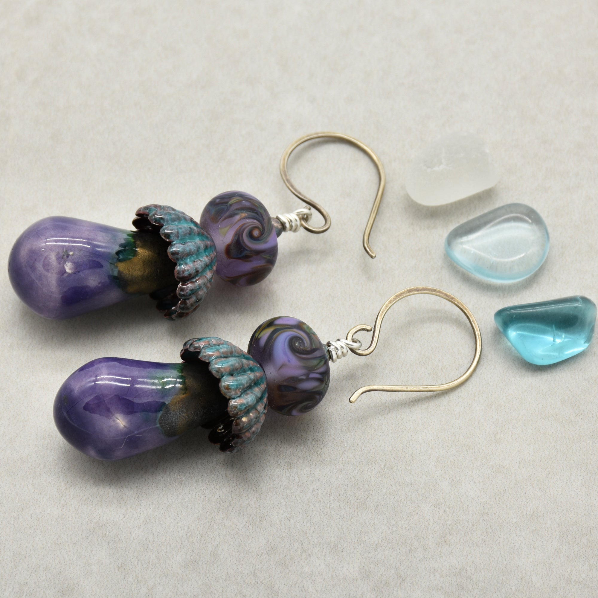 Pair of purple and teal glass bead earrings on a light gray background