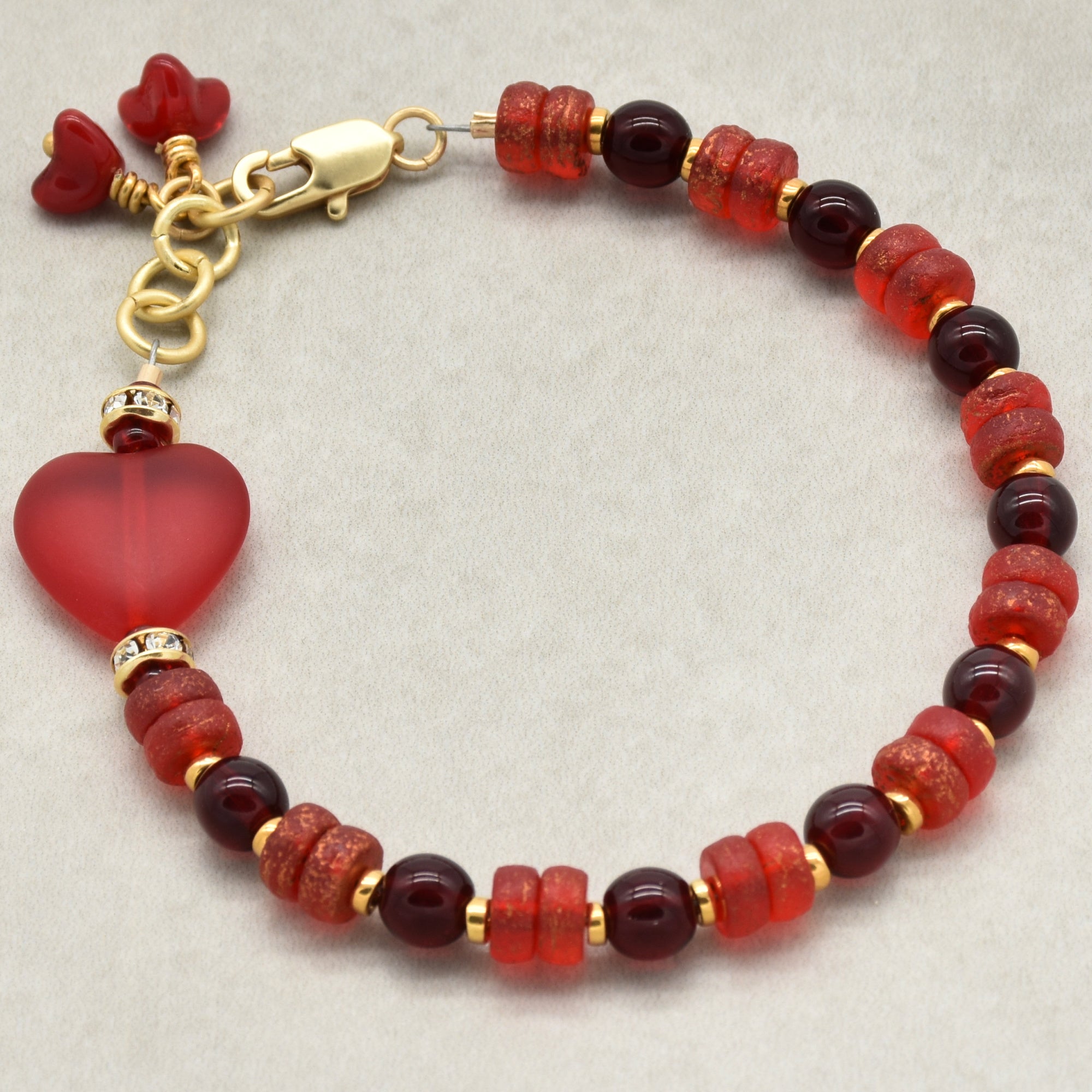 Beaded bracelet with red beads and a heart charm on a light gray background