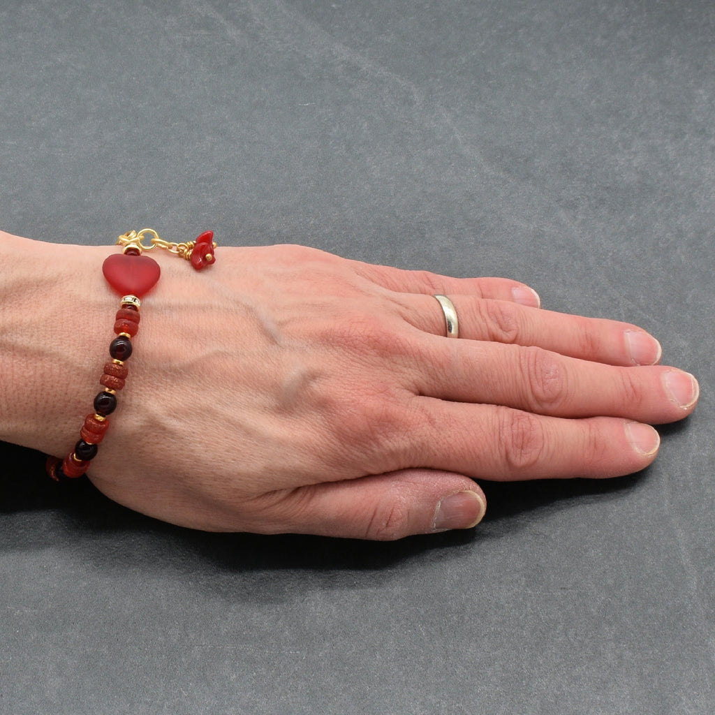 Hand wearing a bracelet with red and gold beads on a gray background