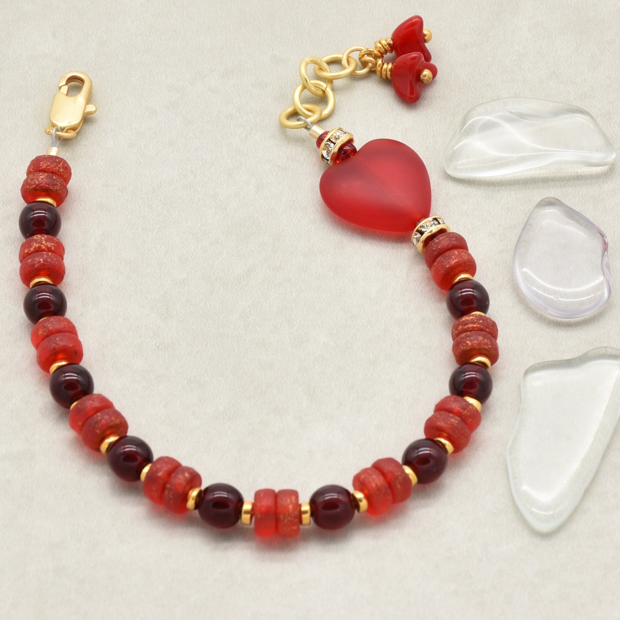 Beaded bracelet with red heart charm on a light gray background