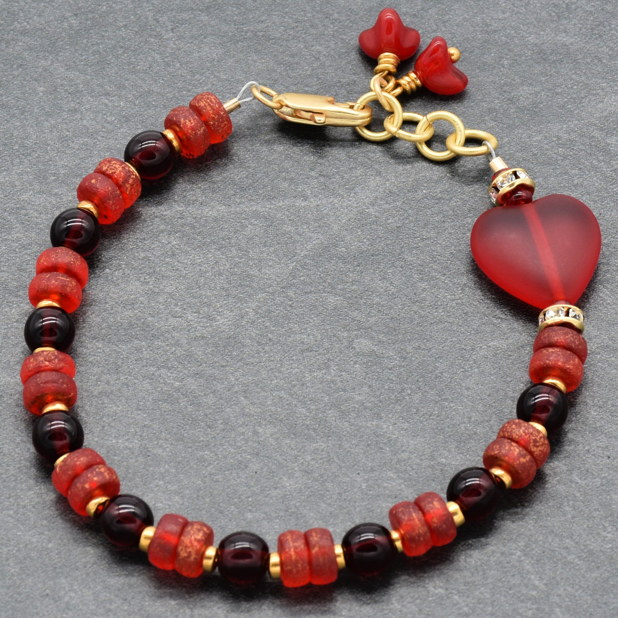 Beaded bracelet with red beads and gold accents on a gray background