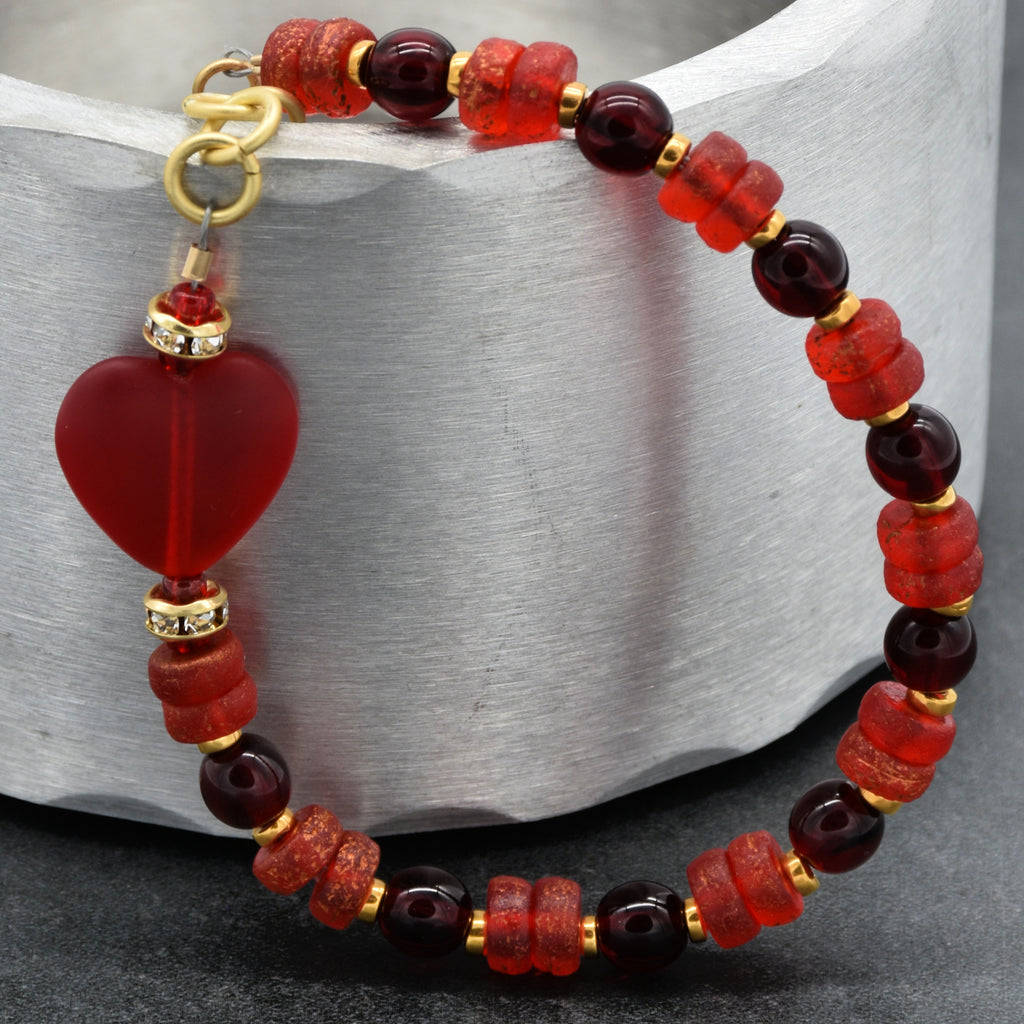 Beaded bracelet with red and gold heart charm on a metallic surface