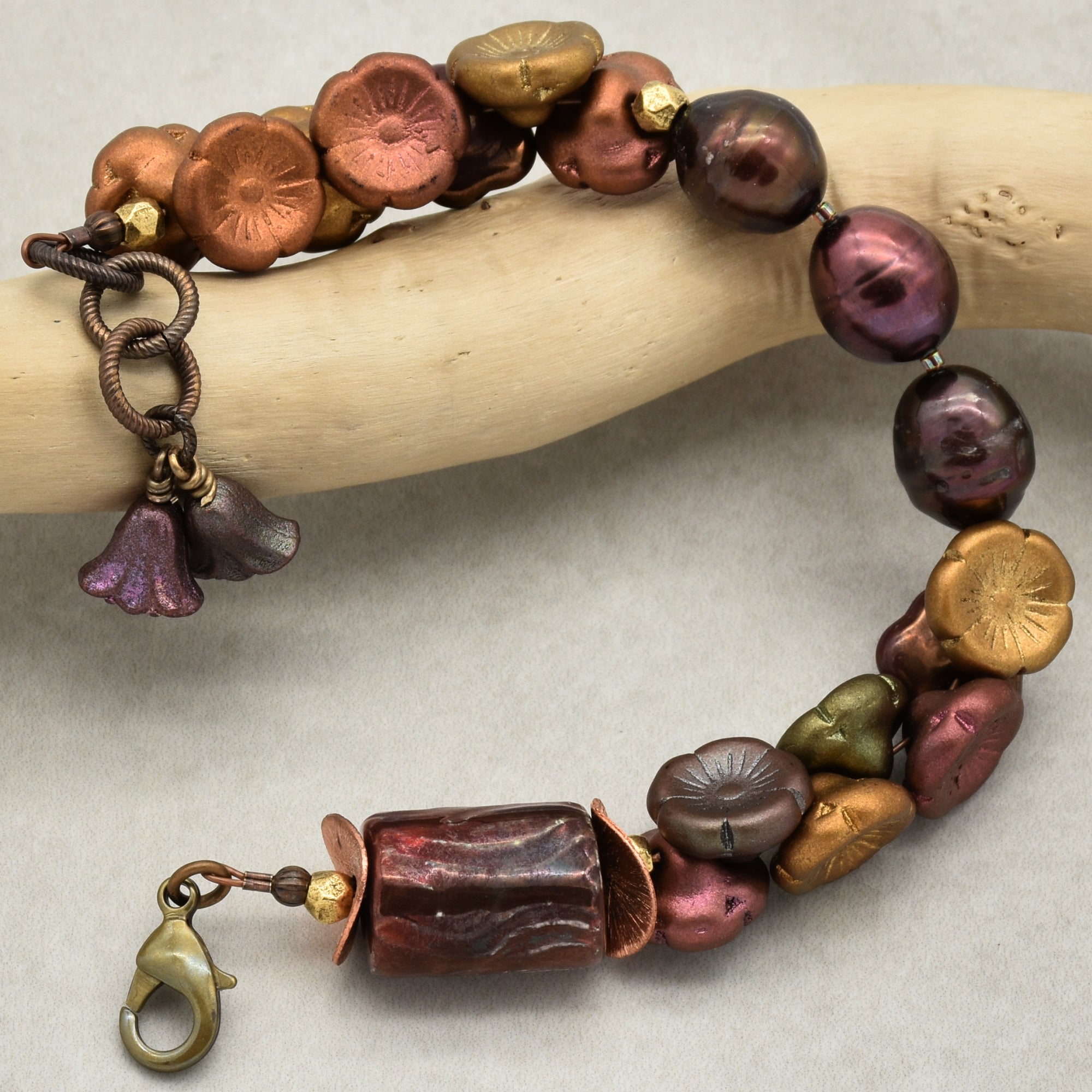 Beaded bracelet with metallic beads on a wooden stick against a neutral background