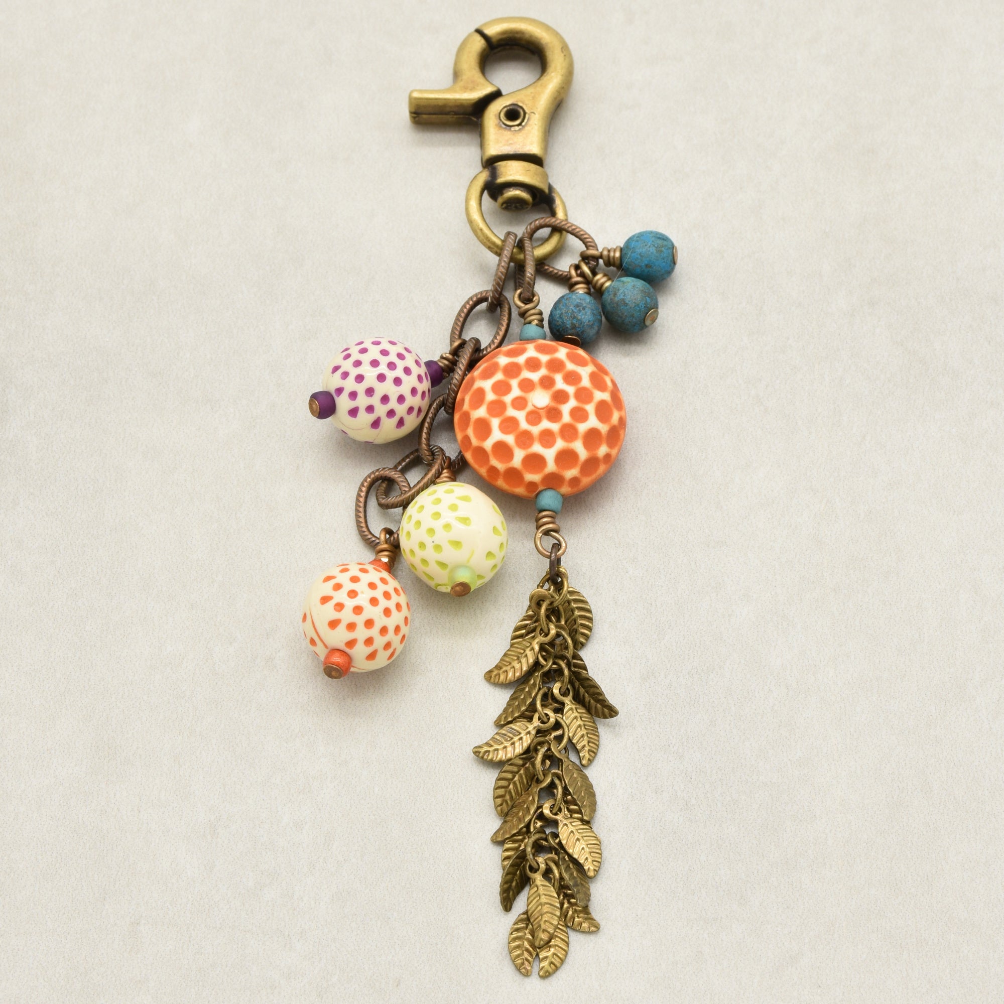 A bohemian-style keychain charm featuring a brass lobster clasp, vintage Lucite beads, Czech glass, and antique brass falling leaves chain, set against a light gray background - made with love in Colorado by Ruby Acorn.