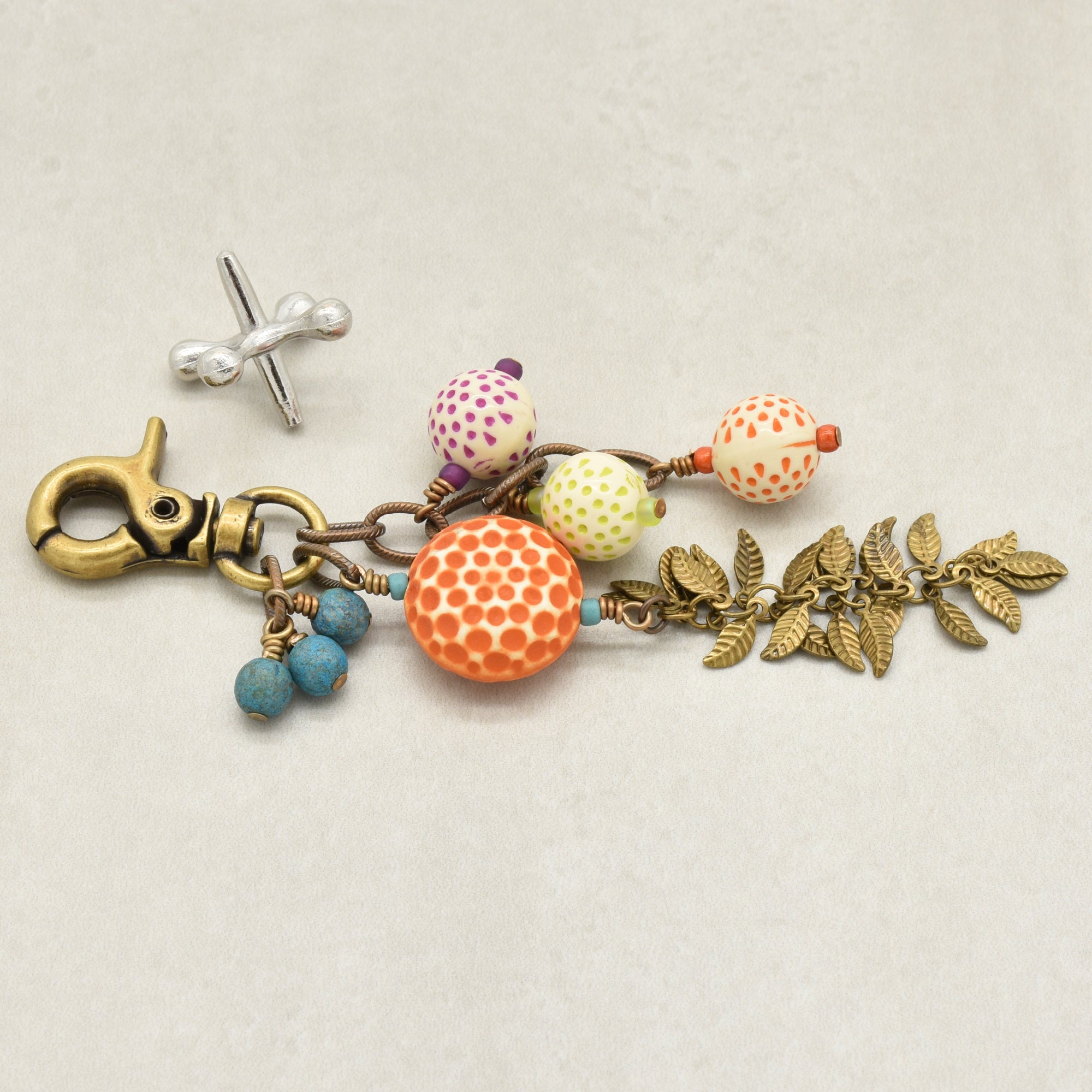 A vintage-style charm keychain with an antique brass-toned lobster clasp, turquoise Czech glass beads, vintage Lucite beads, and antique brass falling leaves chain on a light beige background - made with love in Colorado by Ruby Acorn.