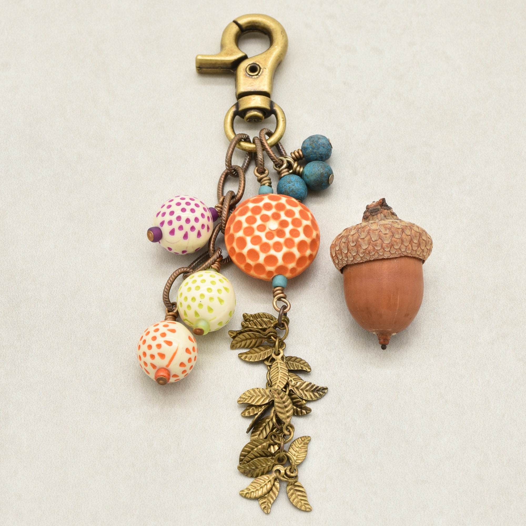 An autumn-themed keychain charm featuring a brass-colored lobster clasp, vintage Lucite beads, Czech glass, and antique brass falling leaves chain, set against a light gray background - made with love in Colorado by Ruby Acorn.