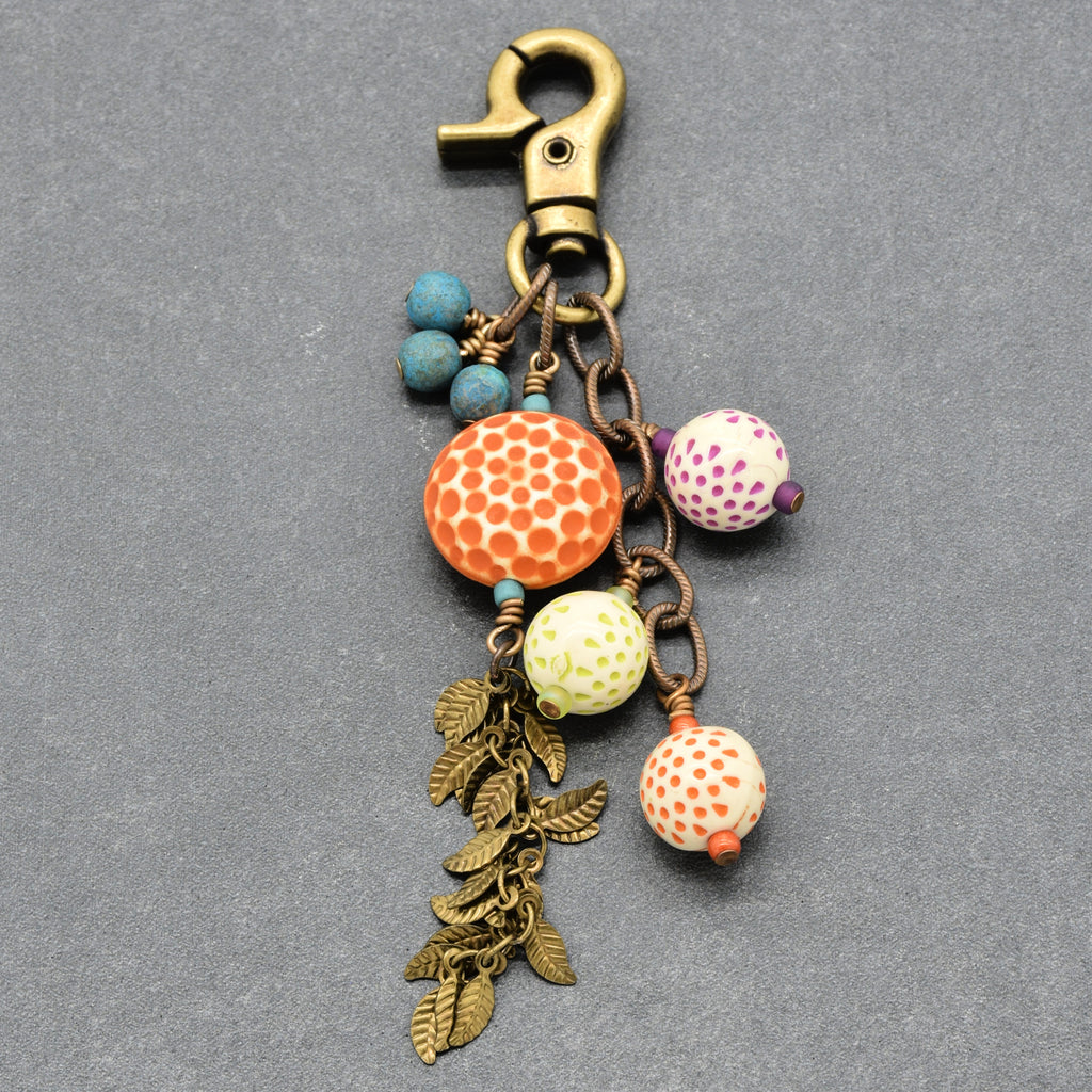 A bohemian-style keychain charm featuring a brass lobster clasp, turquoise Czech glass beads, patterned vintage Lucite beads, and dangling antique brass falling leaves chain, set against a textured gray background - made with love in Colorado by Ruby Acorn.
