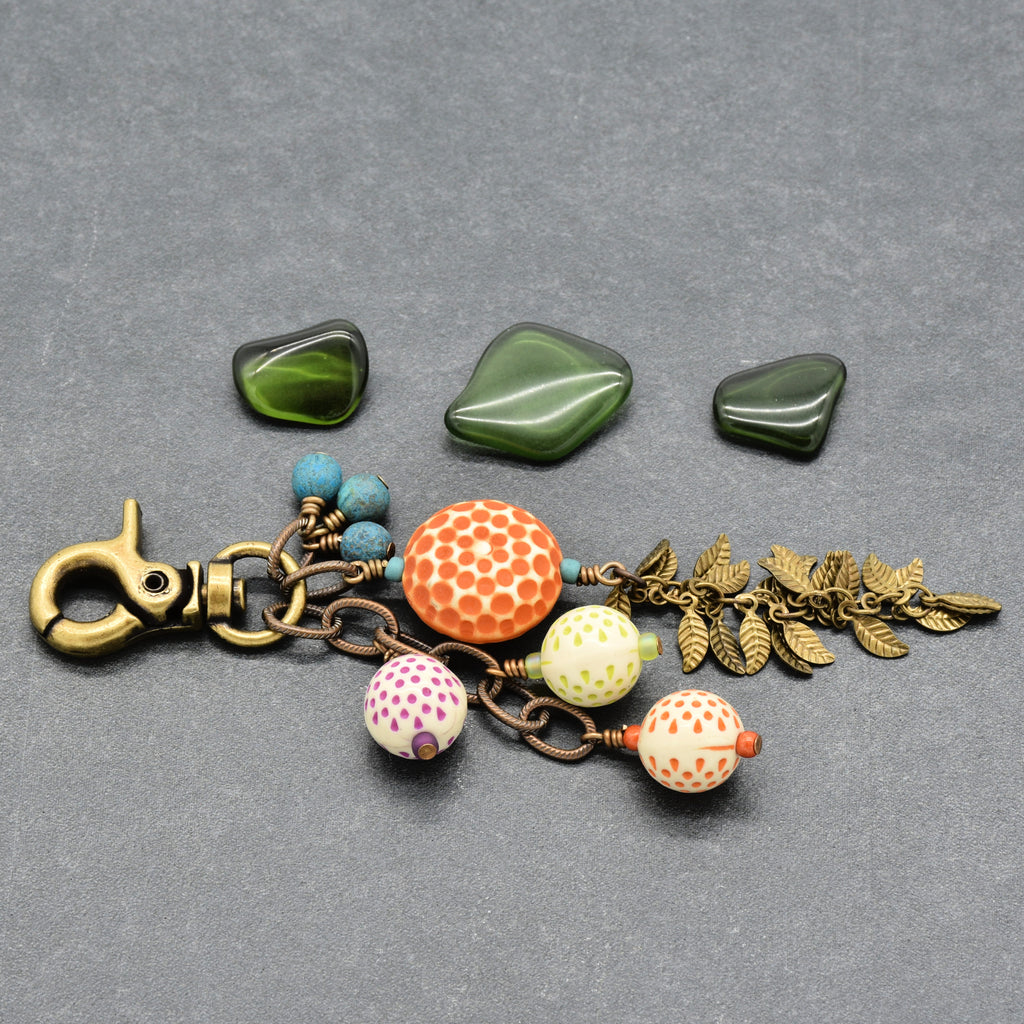 A handmade keychain or bag charm with an antique brass clasp, featuring vintage Lucite, turquoise Czech glass beads, antique brass falling leaves chain on a textured gray background - made with love in Colorado by Ruby Acorn.