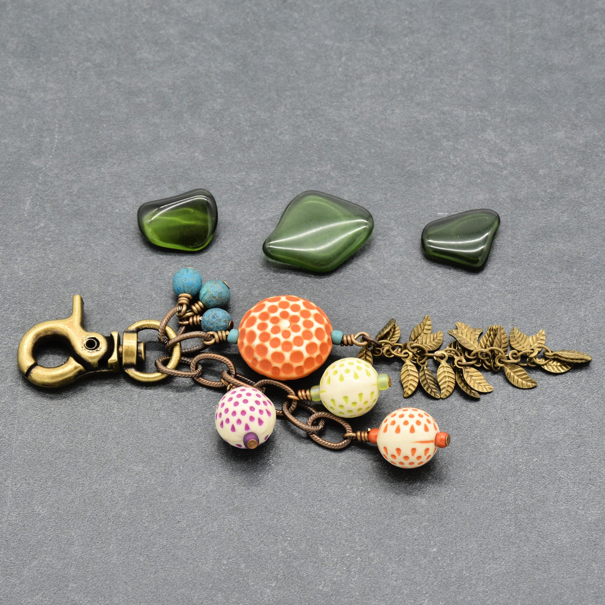 A handmade keychain or bag charm with an antique brass clasp, featuring vintage Lucite, turquoise Czech glass beads, antique brass falling leaves chain on a textured gray background - made with love in Colorado by Ruby Acorn.