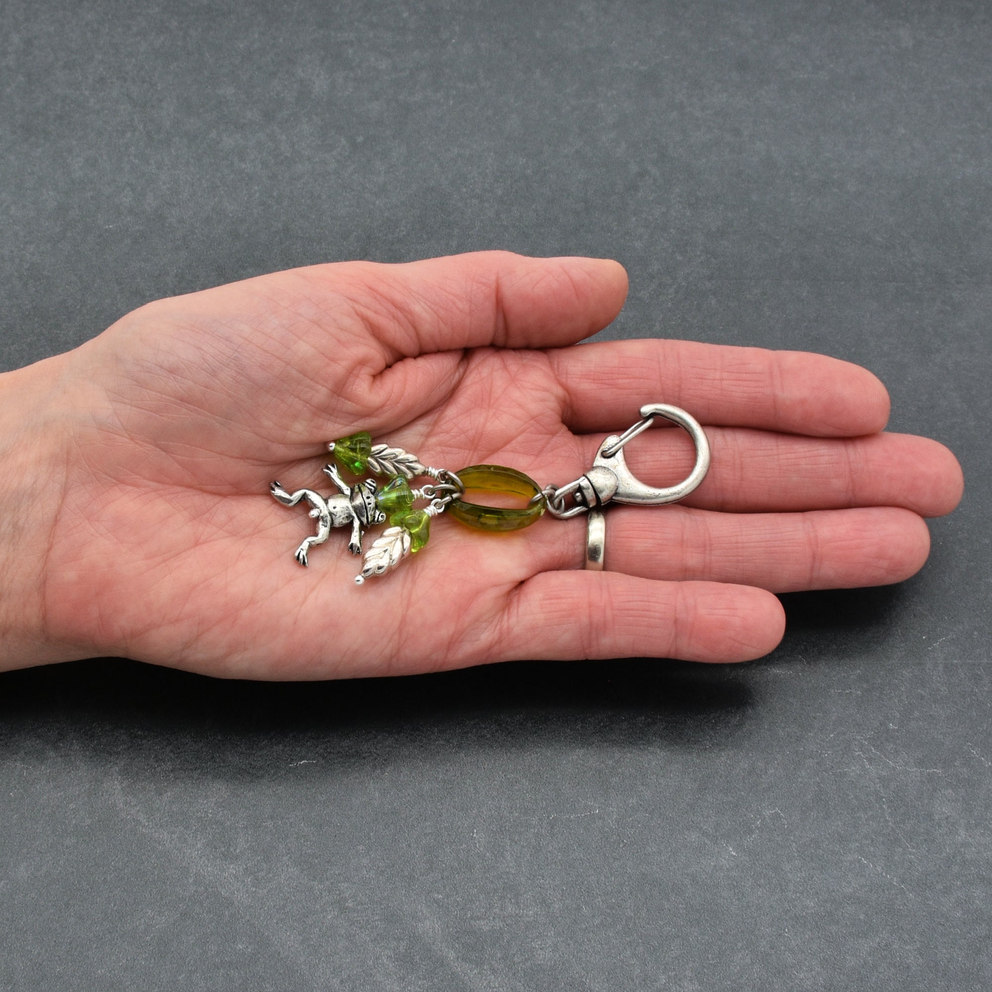 Hand holding a keychain with green and silver charms on a gray background