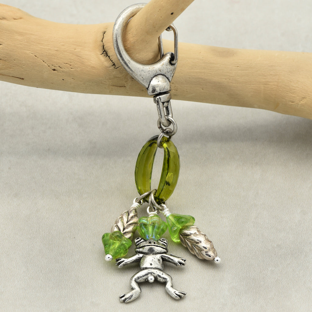 Silver charm with green beads and frog design on a beige background