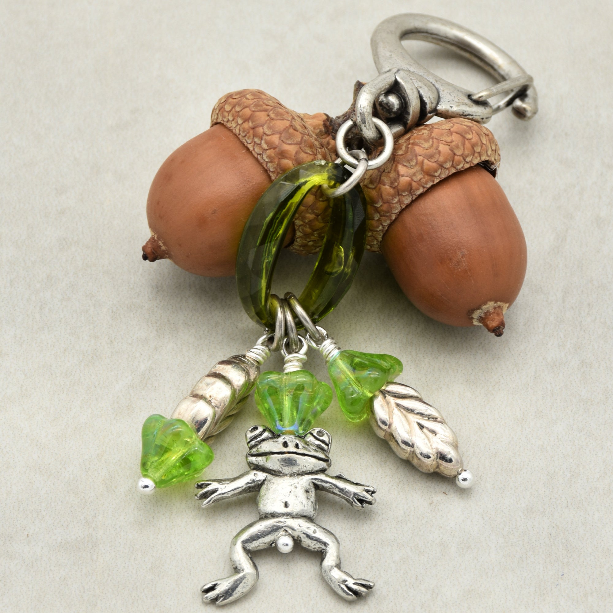 Keychain with acorns, green beads, and a silver frog charm on a light gray background