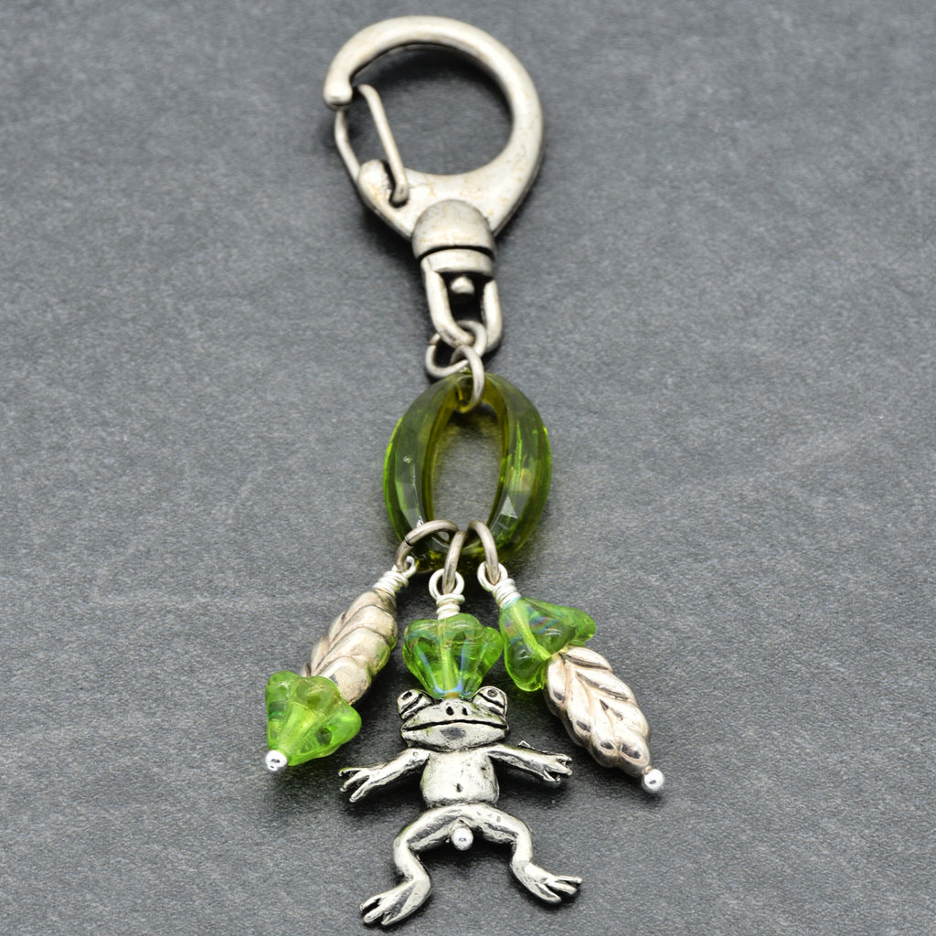 Keychain with silver frog charm, green beads, and a carabiner on a gray background