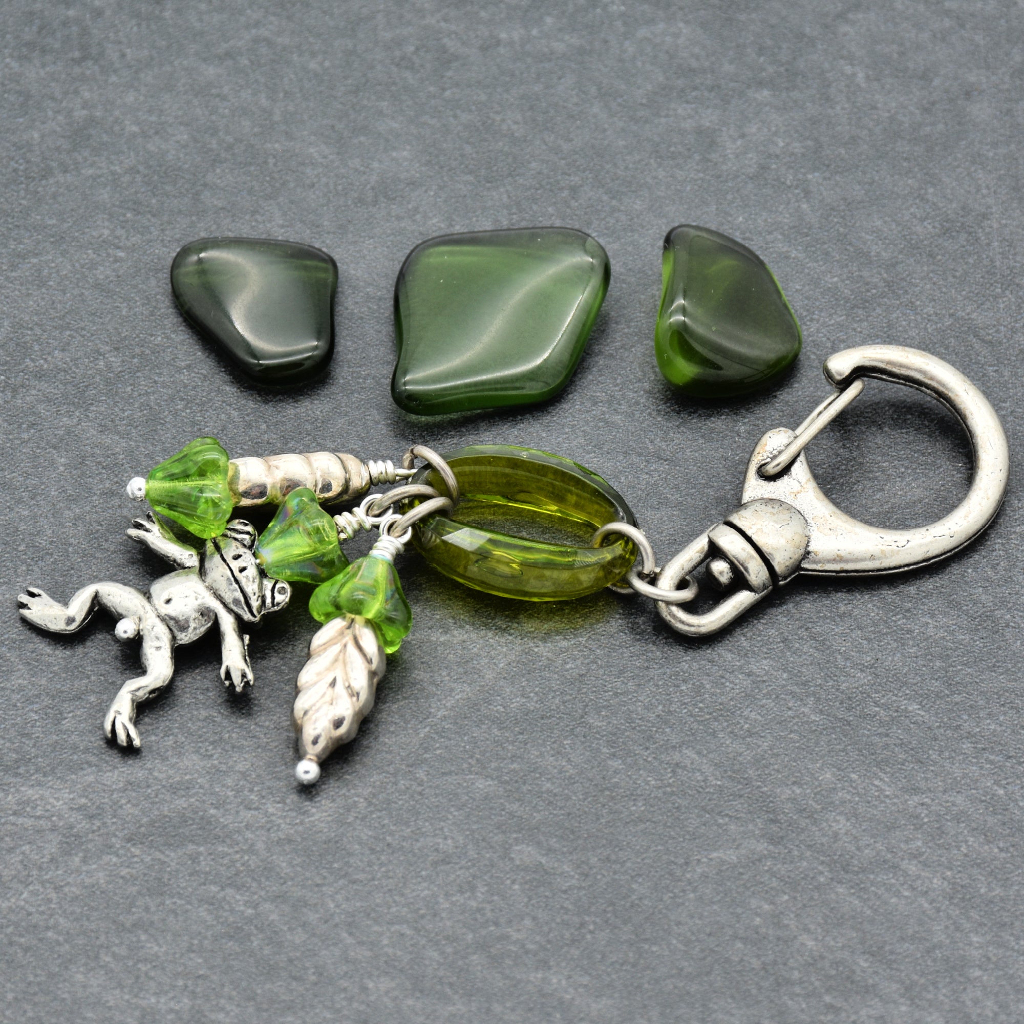 Keychain with green beads and silver frog charm on a gray background
