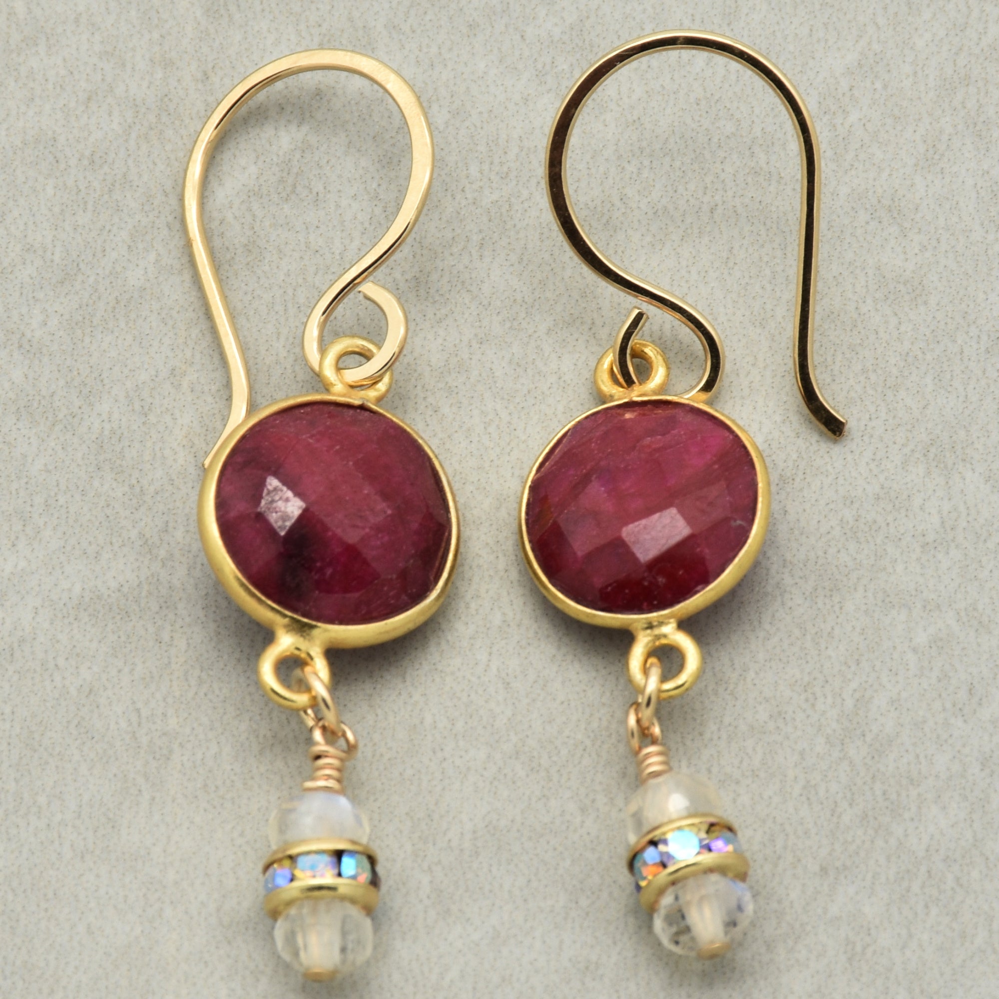 Gold earrings with red gemstones and clear beads on a light gray background