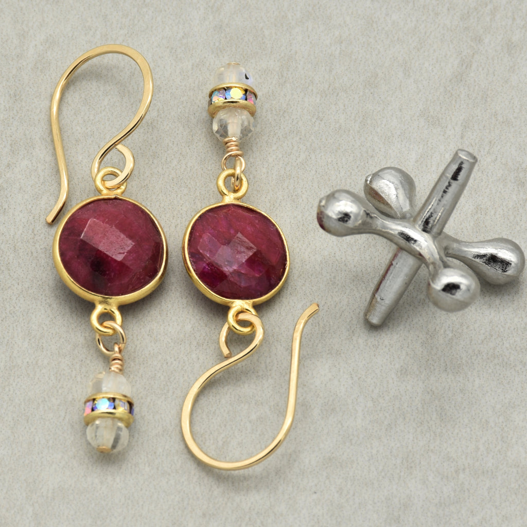 Gold earrings with red gemstones on a gray background