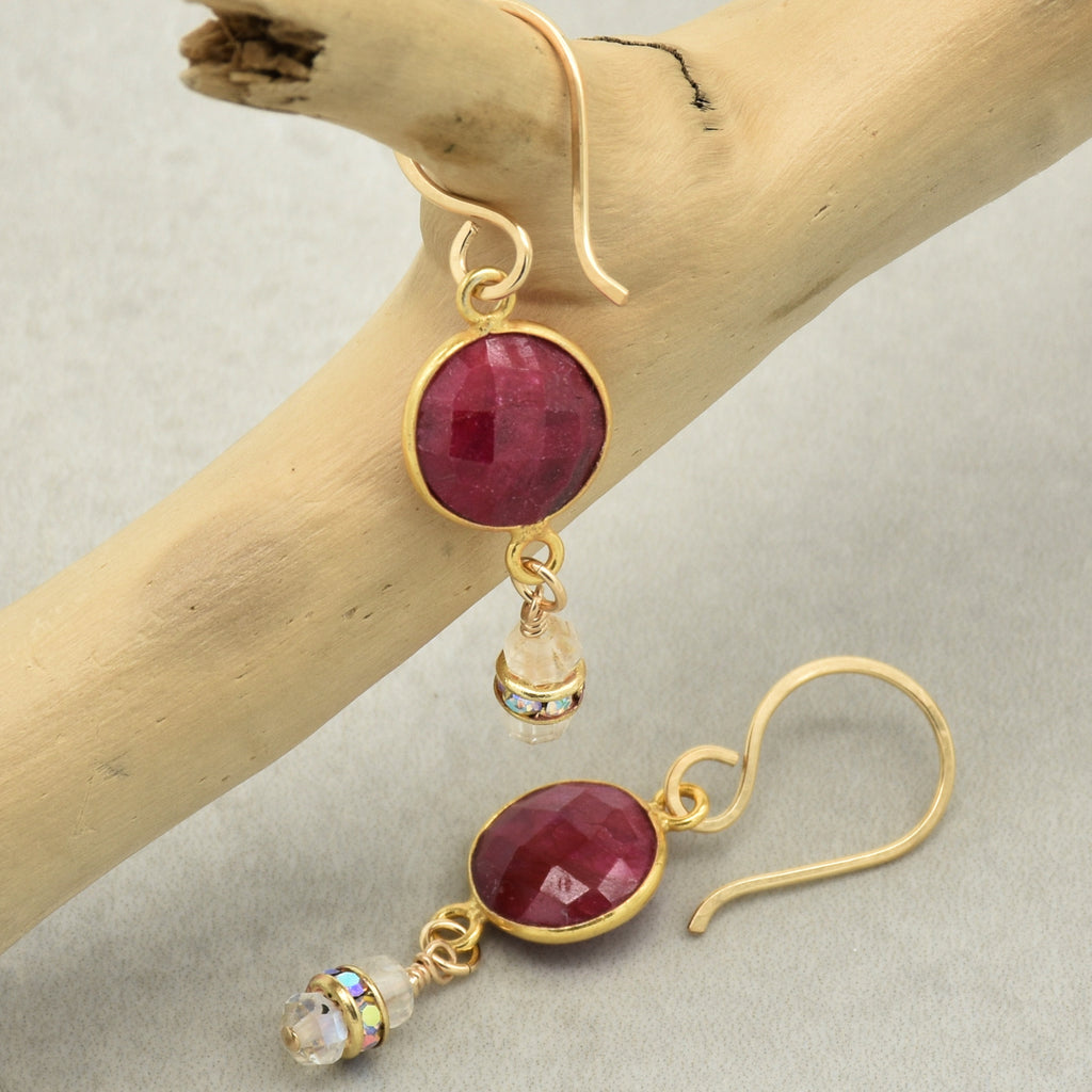 Gold earrings with red gemstones on a wooden branch