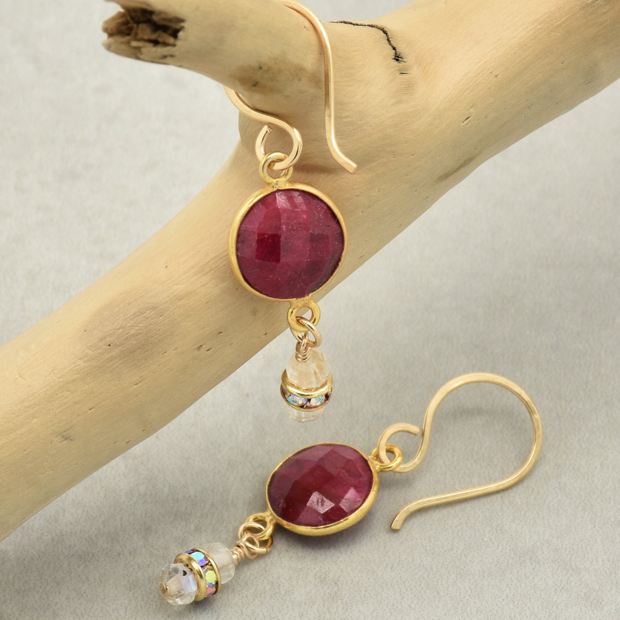 Gold earrings with red gemstones on a wooden branch