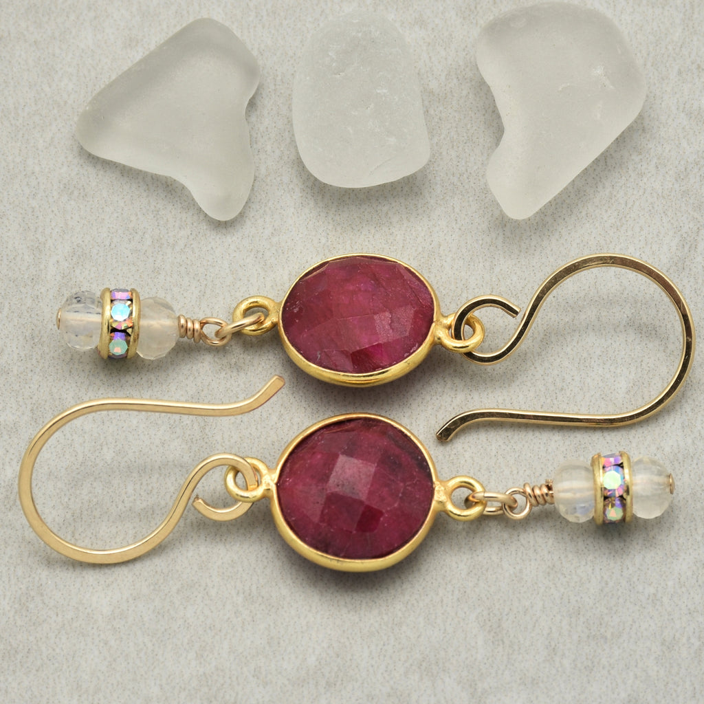 Gold earrings with red gemstones on a textured surface