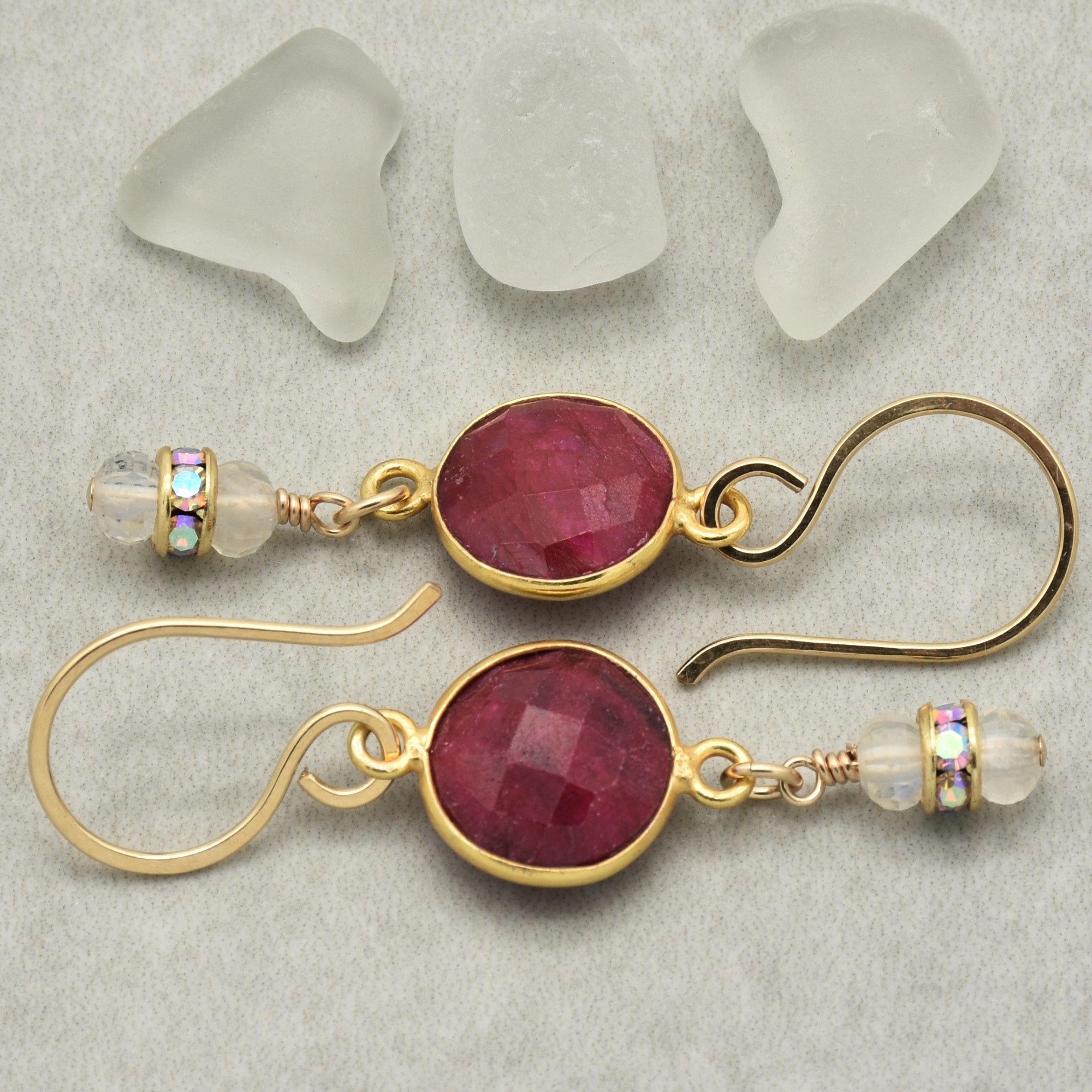 Gold earrings with red gemstones on a textured surface