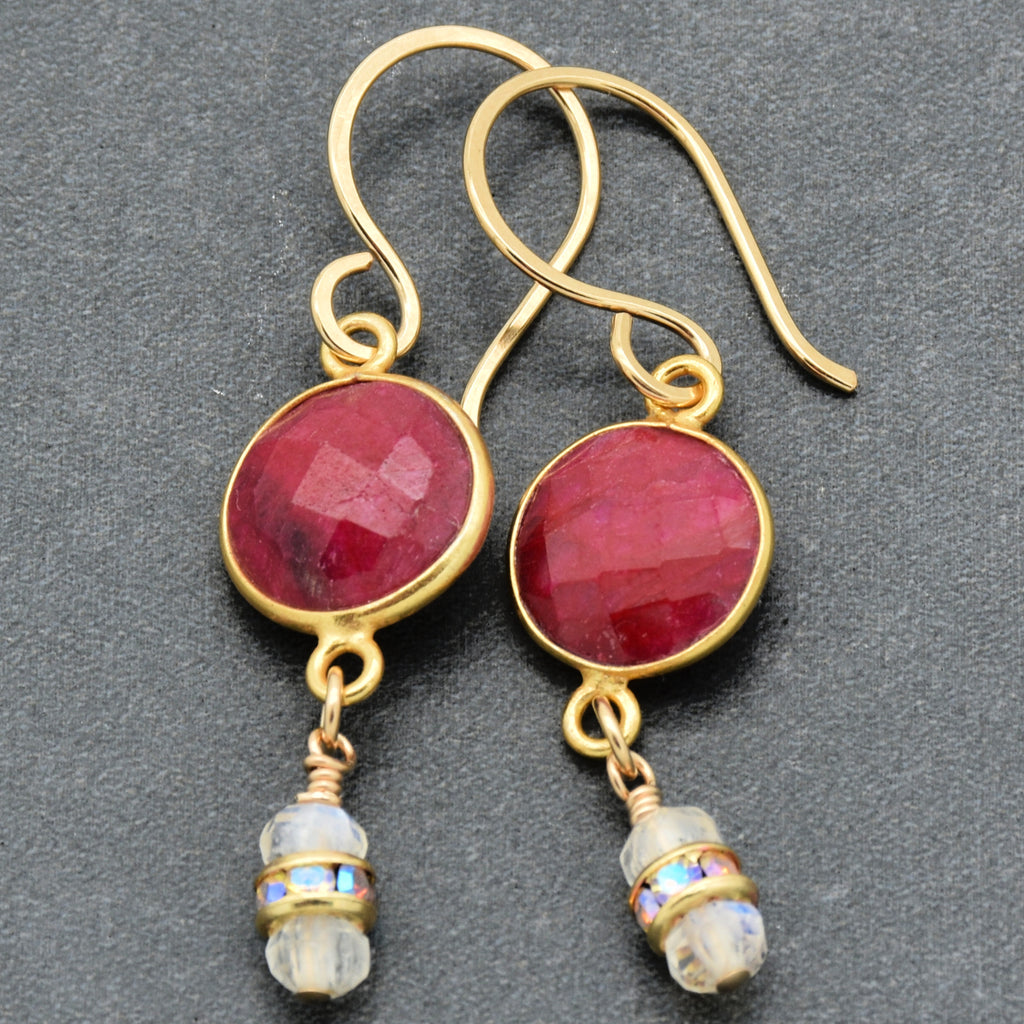 Gold earrings with red gemstones and moonstone drops on a dark background