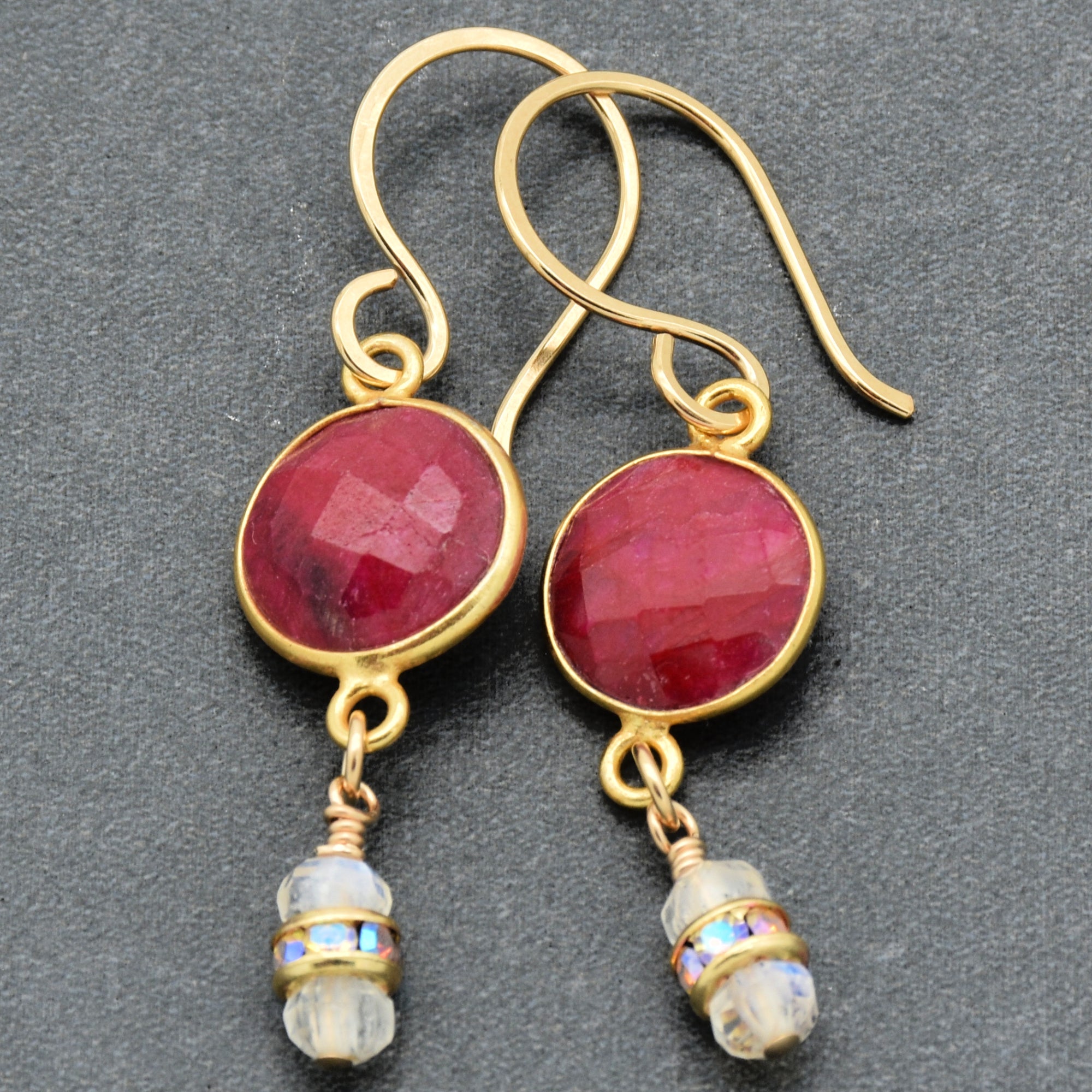 Gold earrings with red gemstones and moonstone drops on a dark background