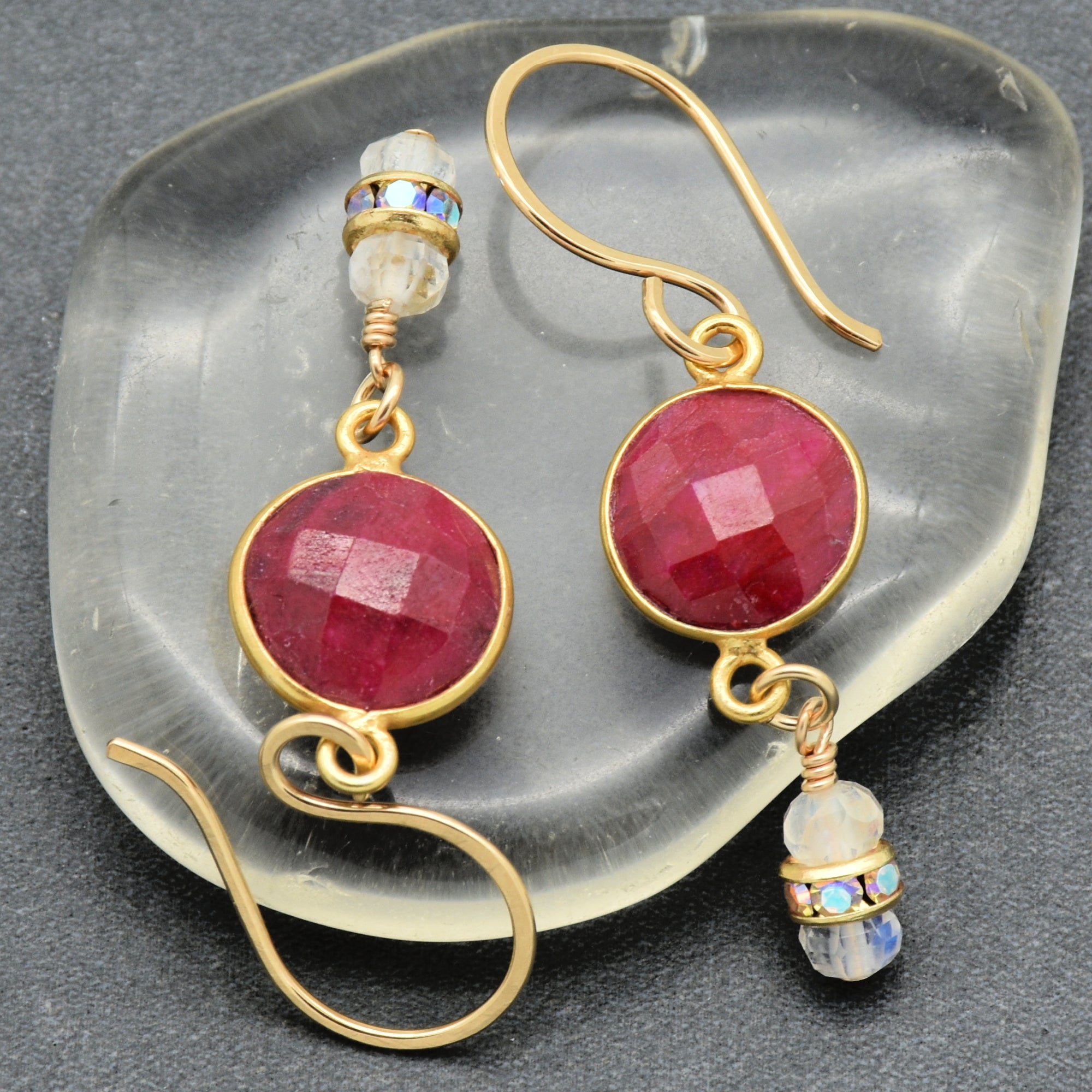 Gold earrings with red gemstones on a clear stone background