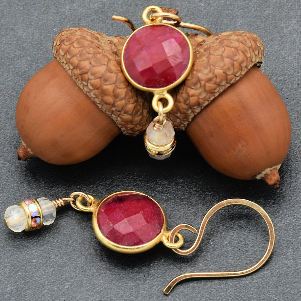 Gold earrings with red gemstones on acorns against a dark background