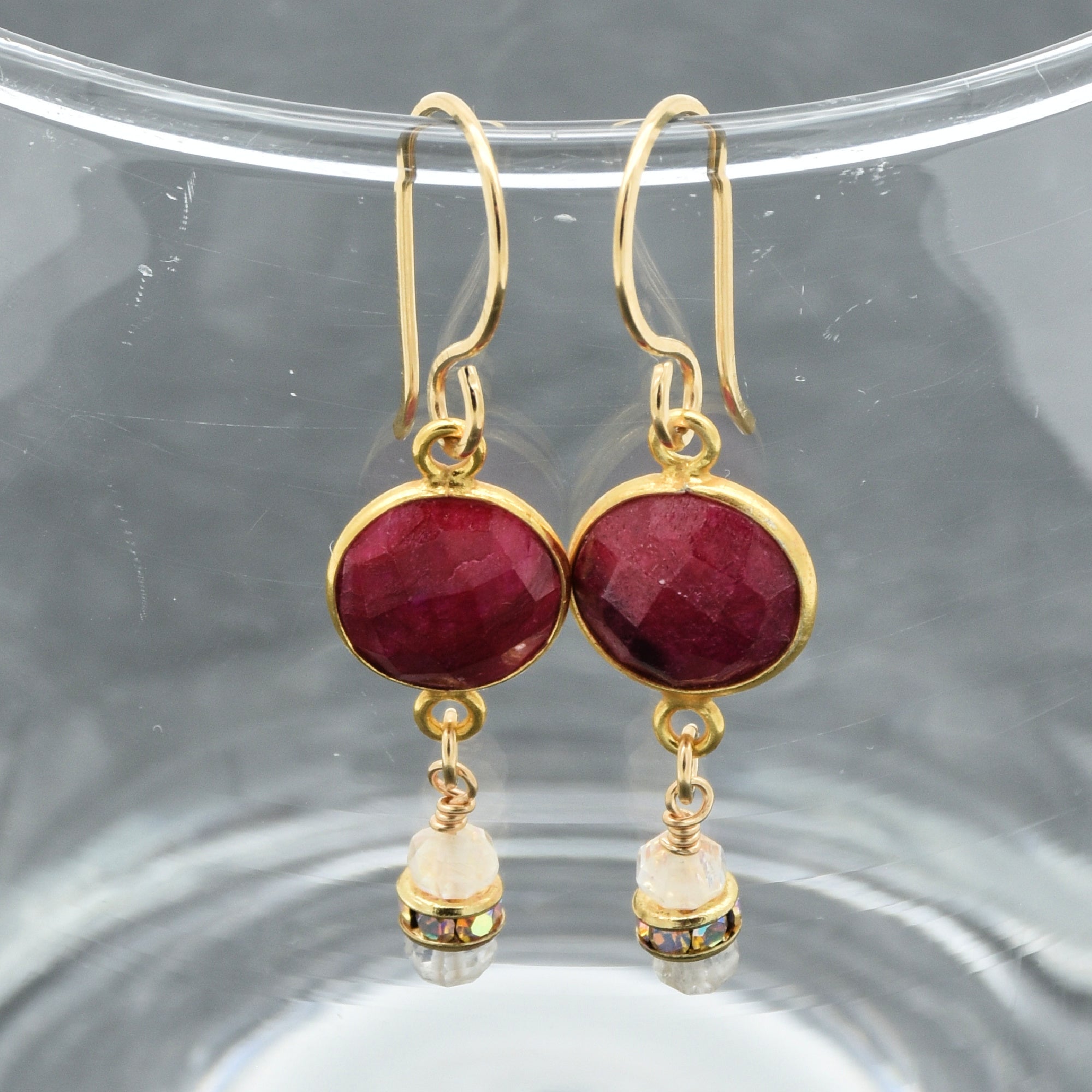 Gold earrings with red gemstones on a clear stand