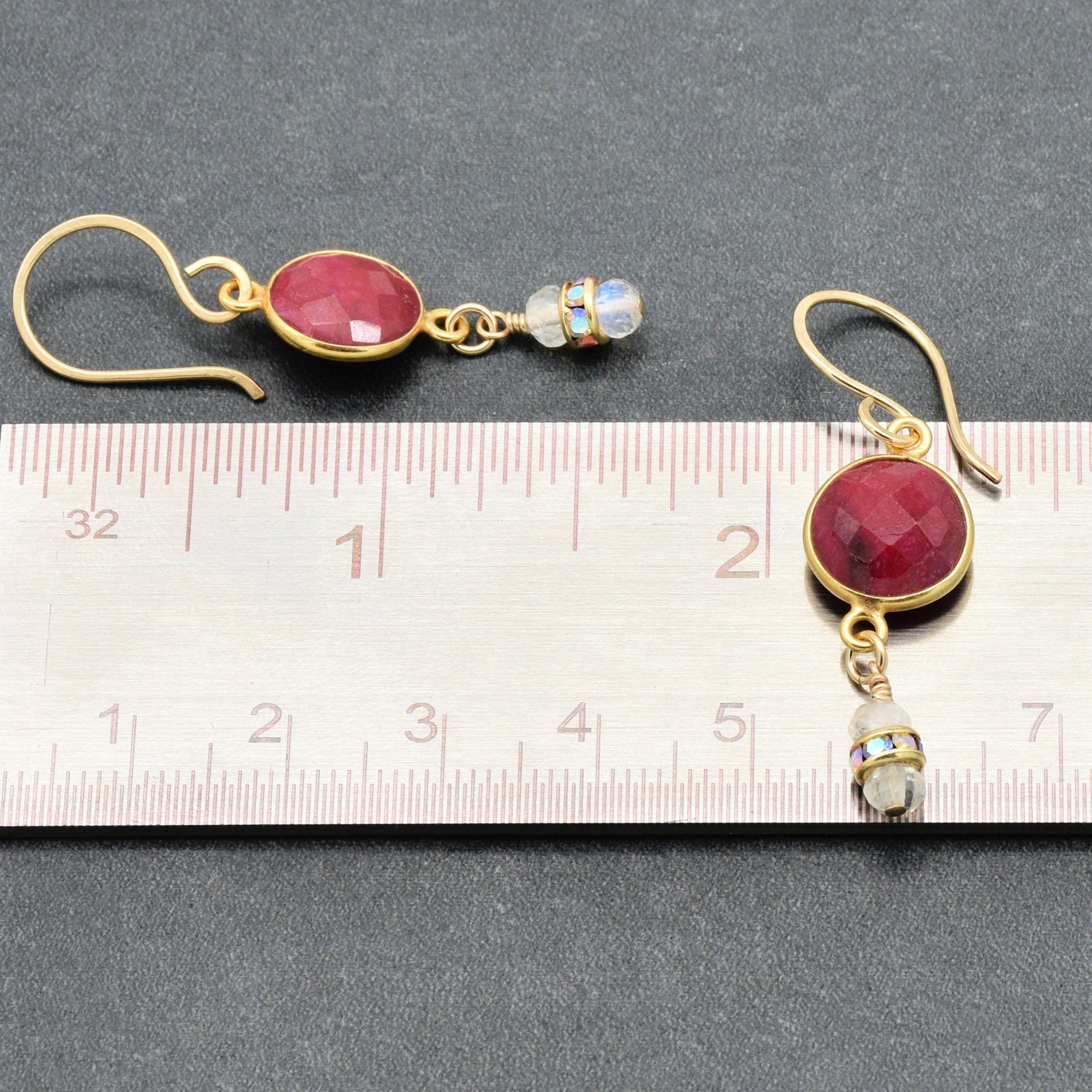 Gold earrings with red gemstones on a ruler for scale