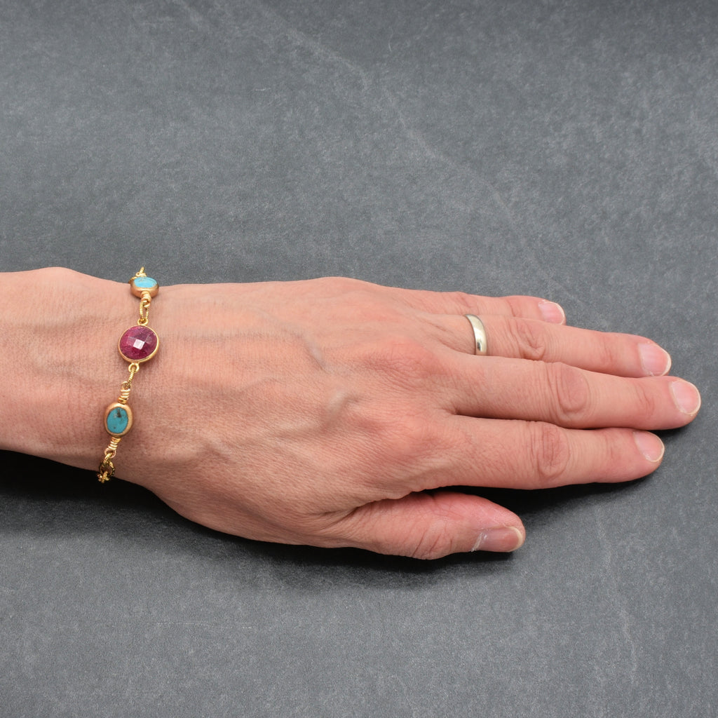 Hand wearing a gold chain bracelet with ruby and turquoise - handmade with love in Colorado by Ruby Acorn