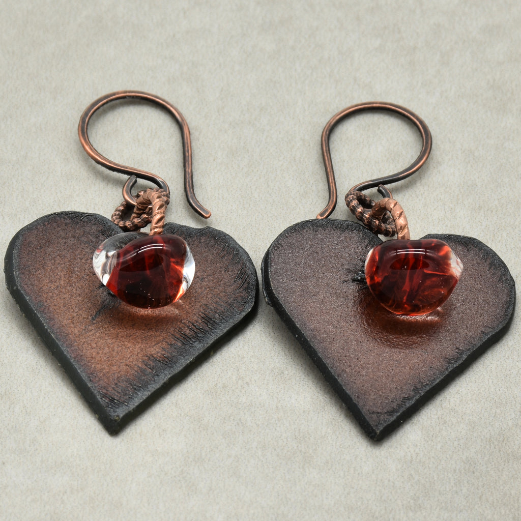 Heart-shaped earrings with red glass charms on a beige background