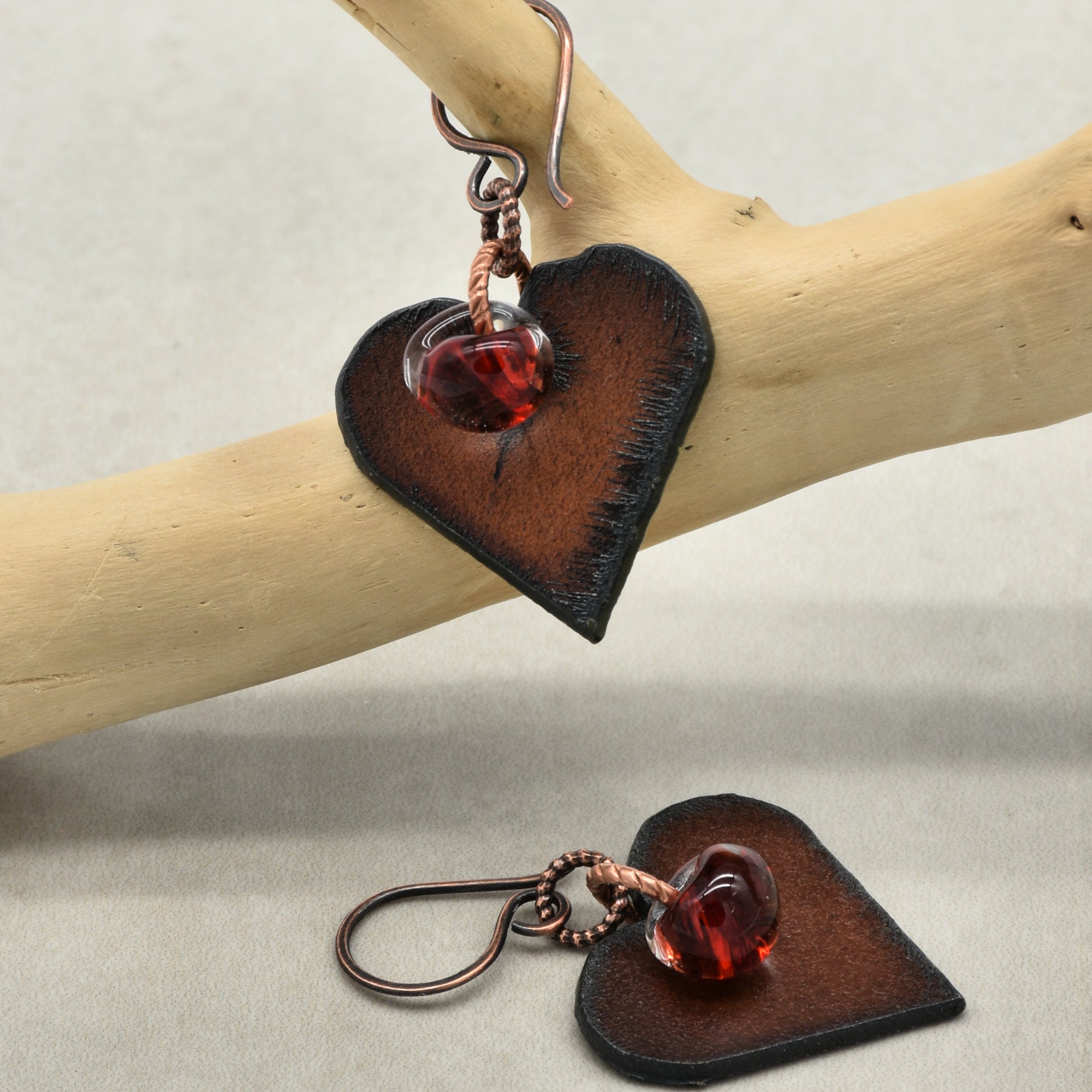 Heart-shaped earrings with red lampwork teardrps on a wooden branch