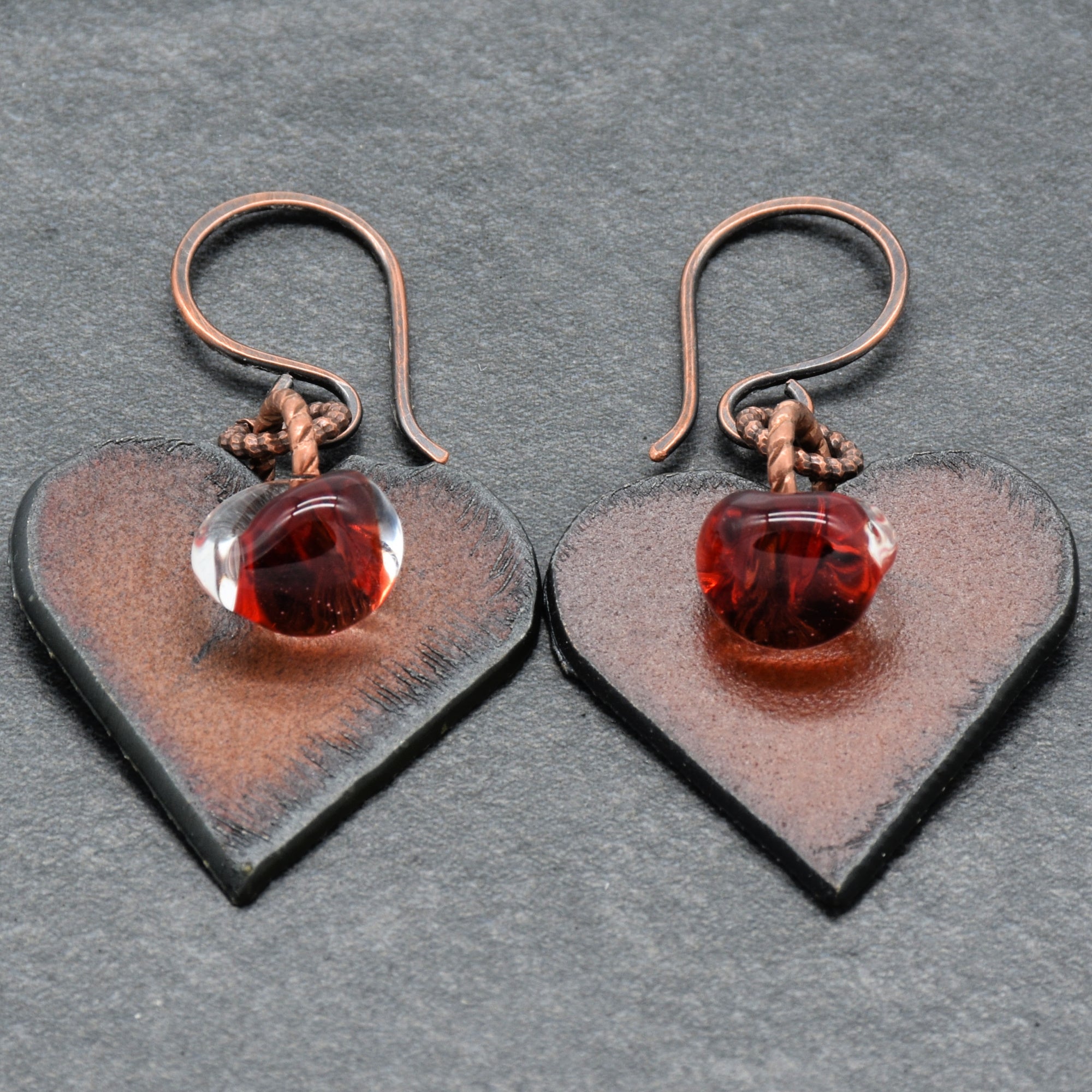 Heart-shaped earrings with red glass charms on a gray background