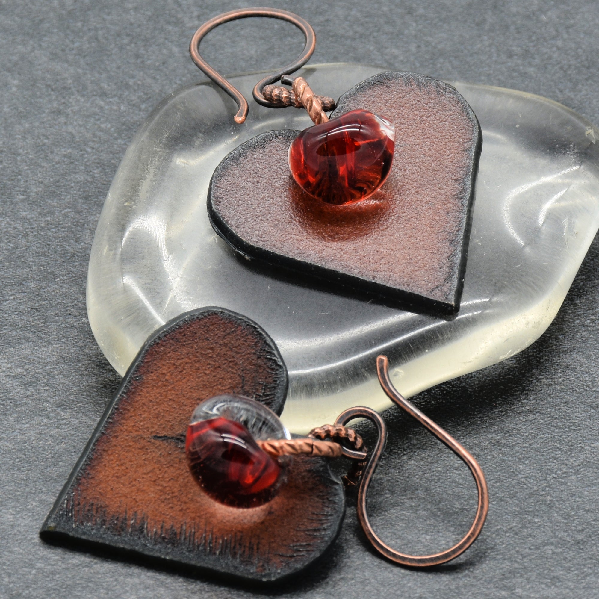Heart-shaped earrings with red lampwork teardrops on a gray surface