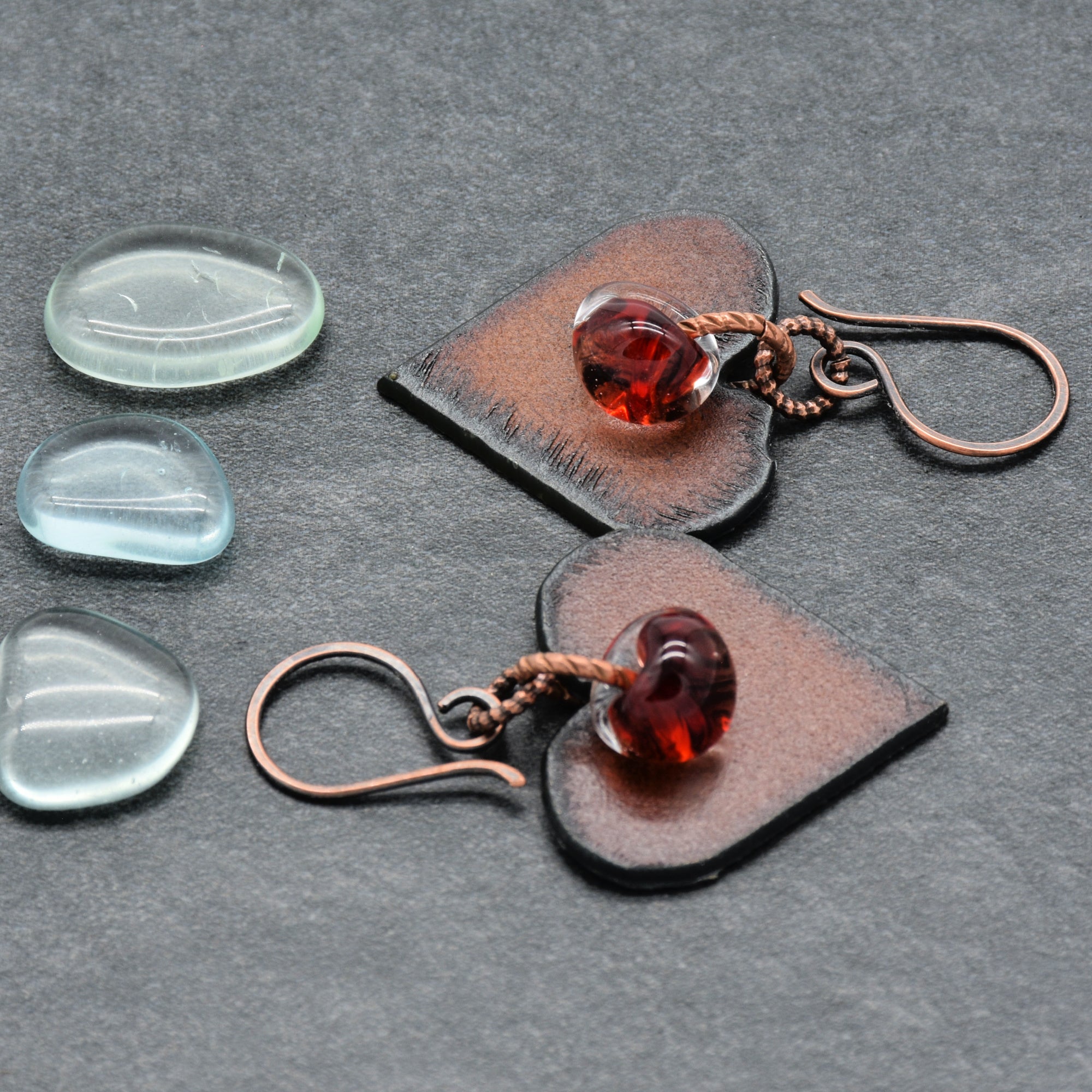 Heart-shaped earrings with red lampwork teardrops on a gray background