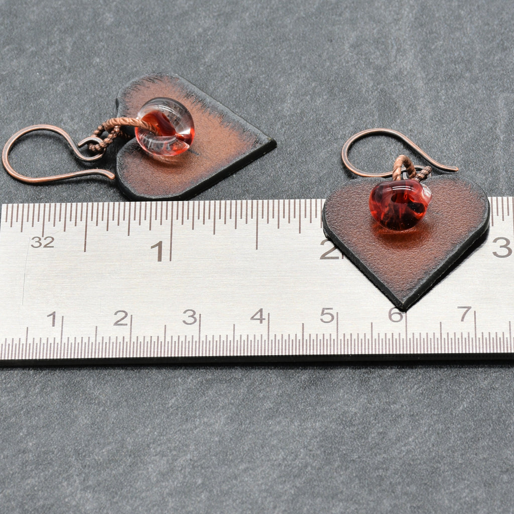 Heart-shaped earrings with red charms on a ruler for scale