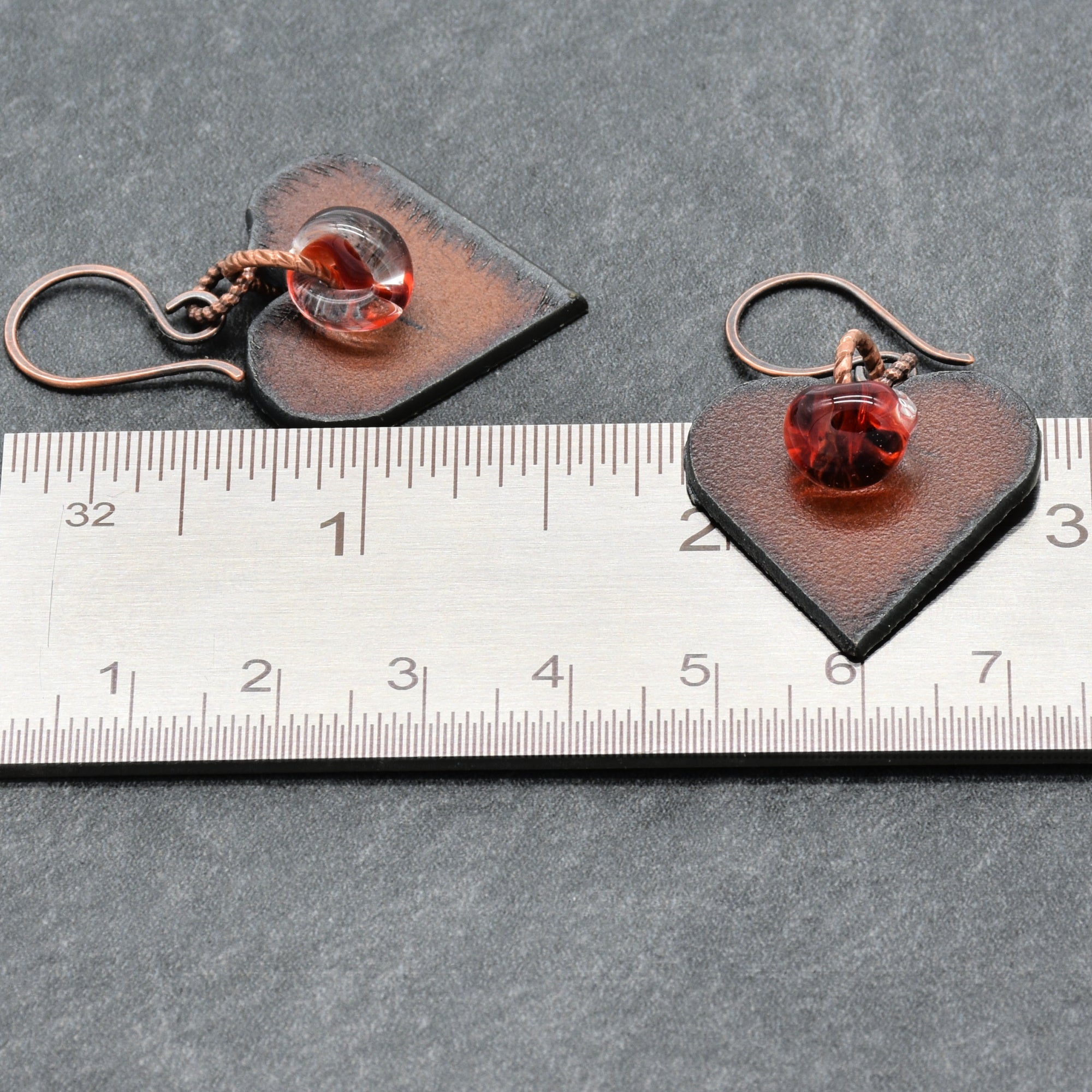 Heart-shaped earrings with red charms on a ruler for scale