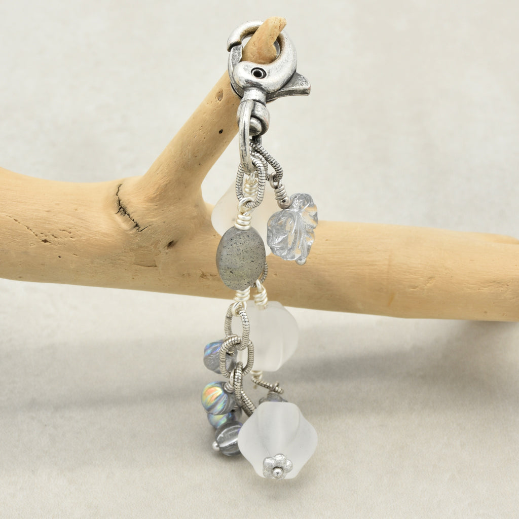 Snowfall Serenade handmade bag charm with three frosted white fluted Lucite beads, a labradorite oval, gray Czech glass beads, a clear glass maple leaf, and an antique-silver-finish swivel clasp on a branch.