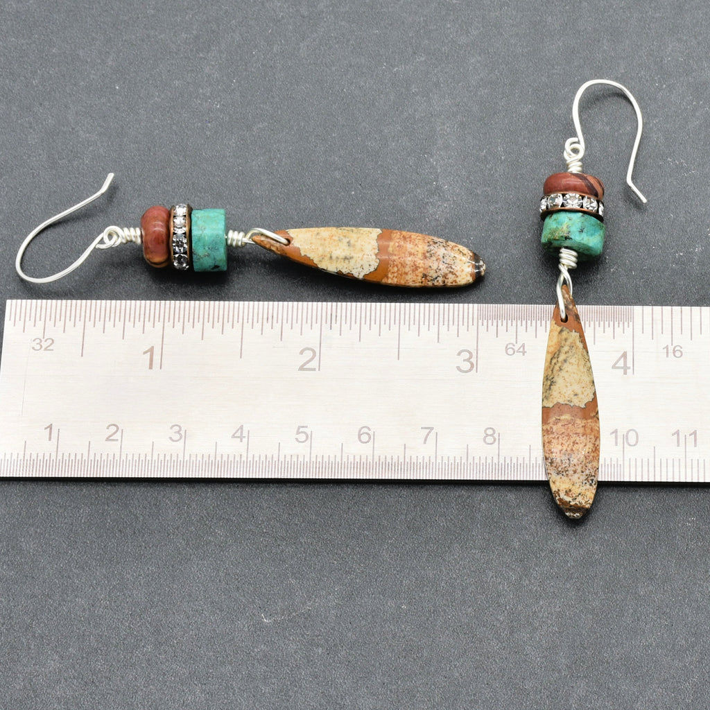 These are earrings. The image shows two pieces of jewelry with hooks at the top, which are typical for earrings. The ruler also helps to see their size, which is consistent with earrings.