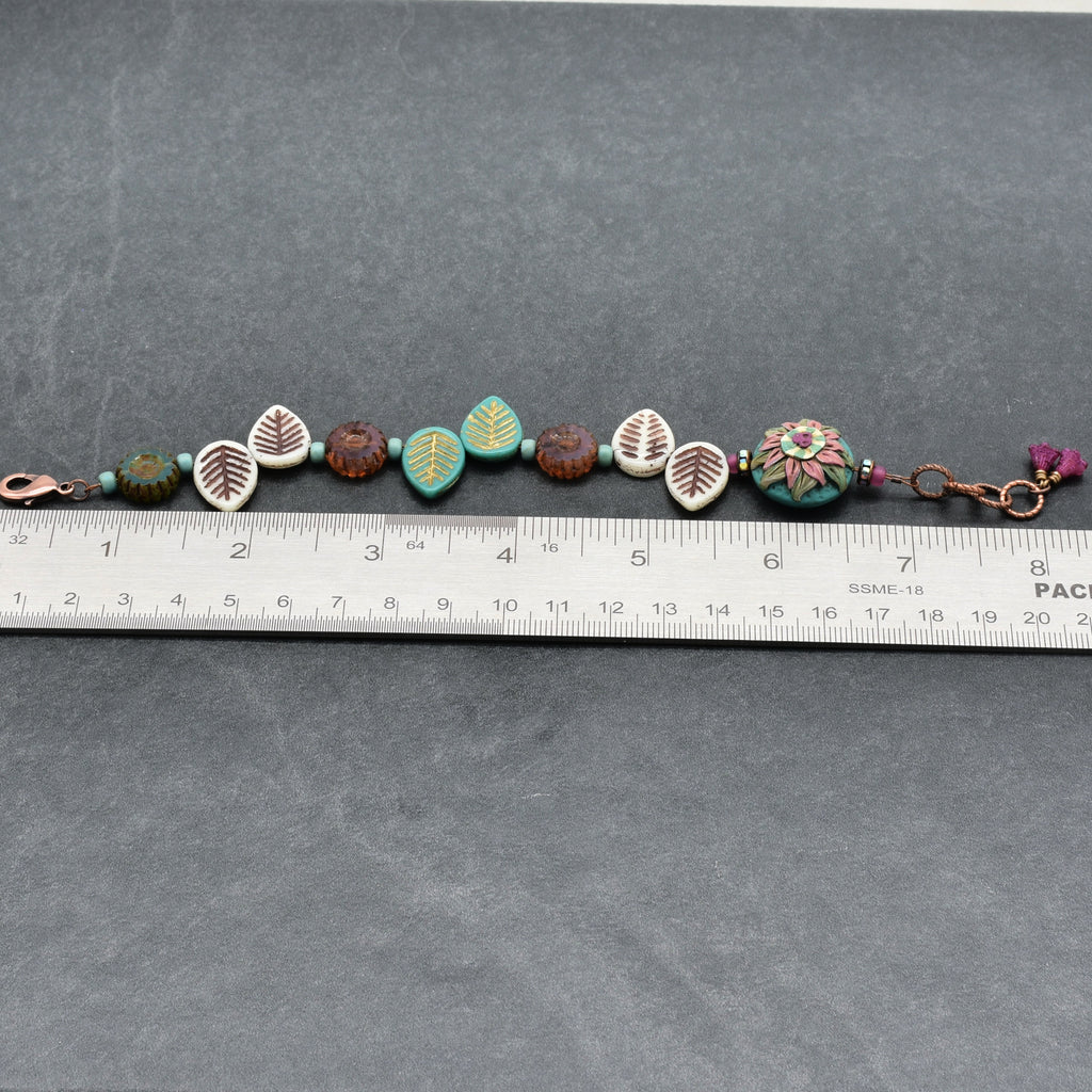 Beaded bracelet with decorative elements on a gray surface with a ruler for scale.